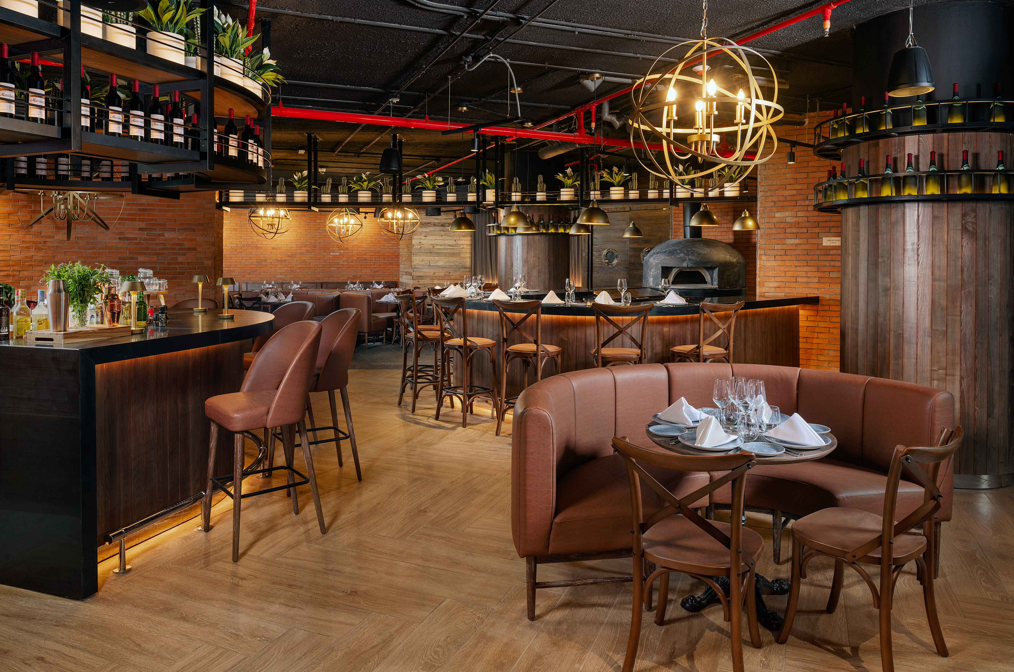Restaurant interior with brick walls, wood bar, wine display, and pizza oven.