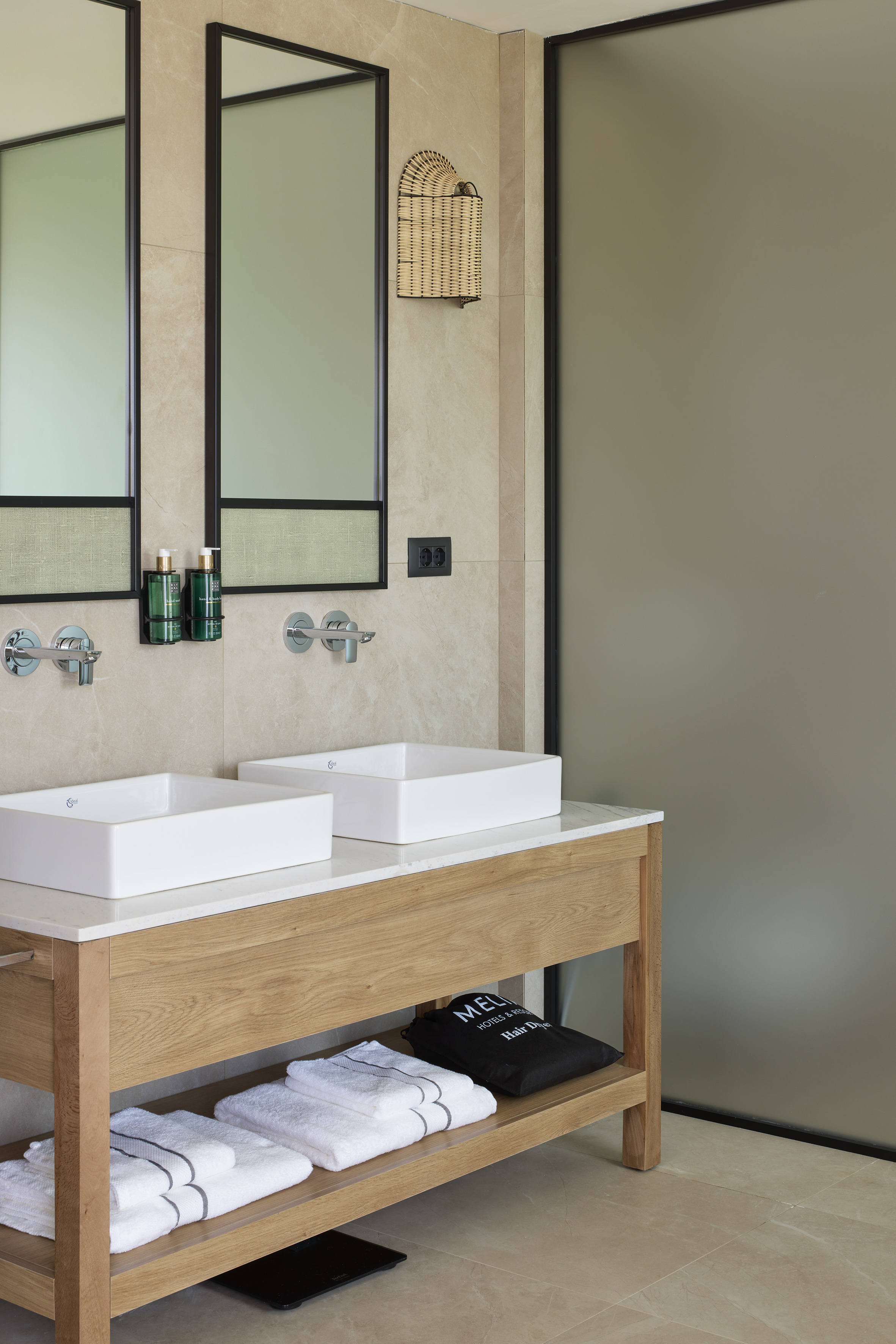 Modern hotel bathroom with wooden dual vanity, white sinks, and framed mirrors.