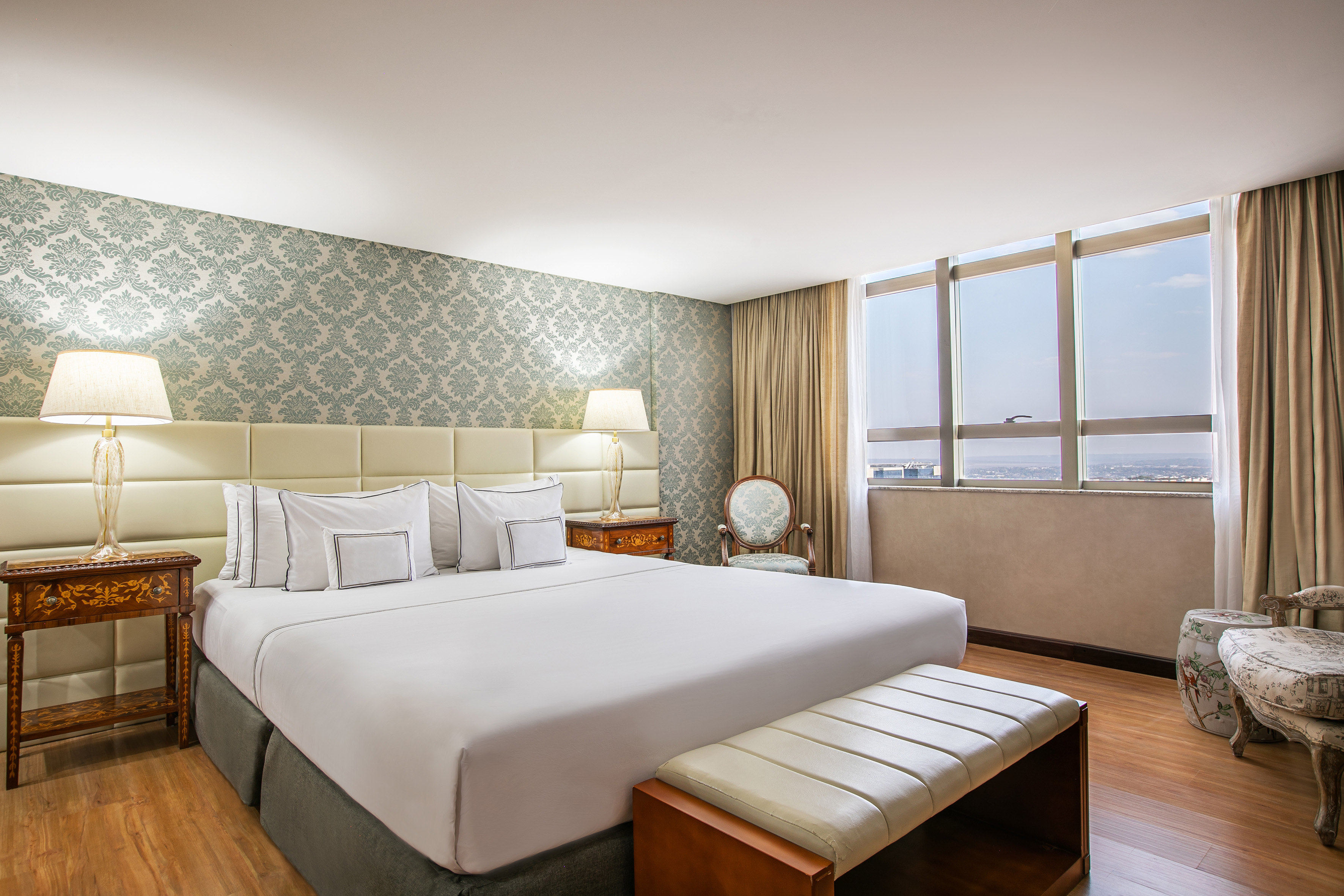 Elegant hotel bedroom with king bed, patterned wallpaper, and city view window.