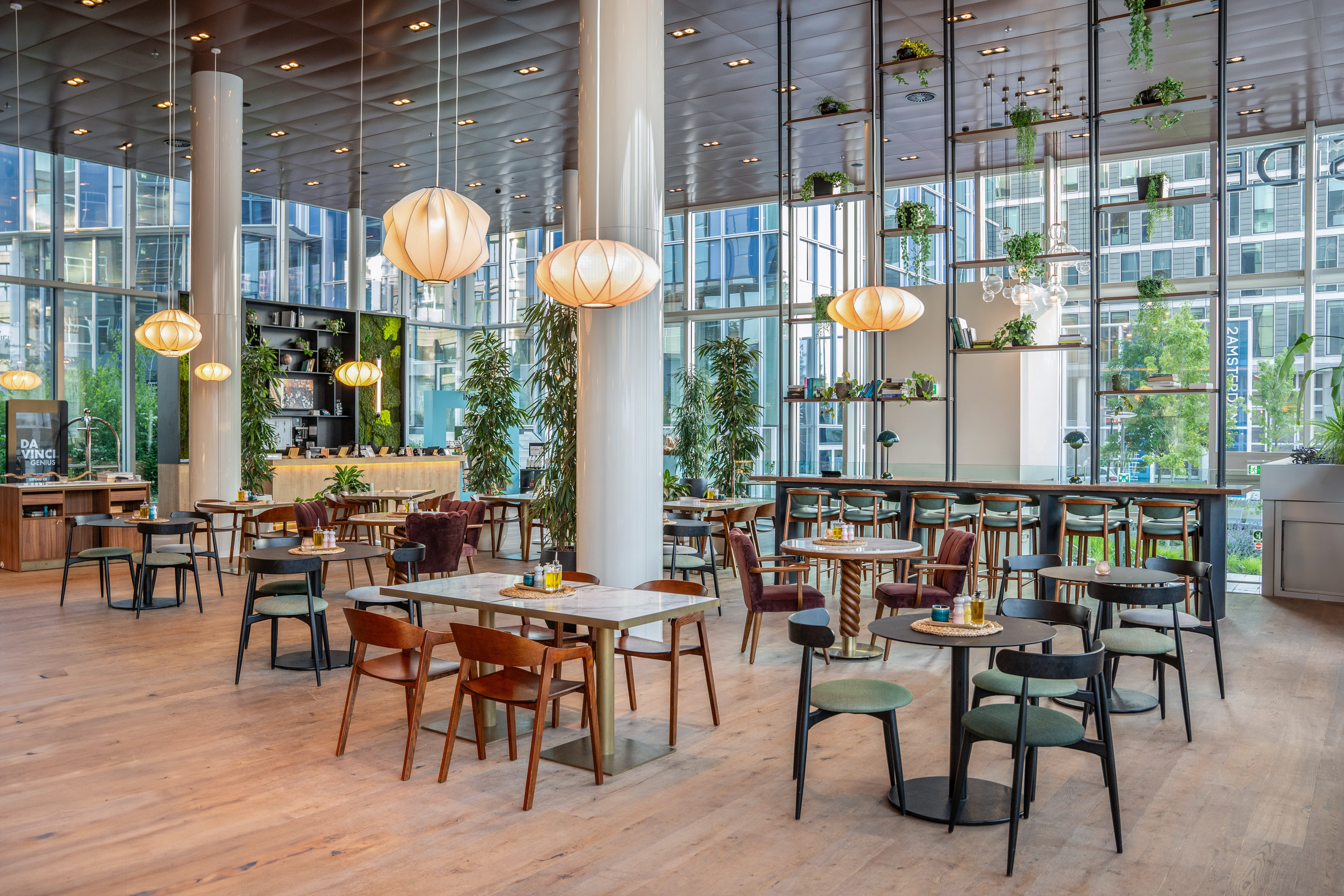 Modern cafe lounge with diverse seating, large windows, and lush plants.