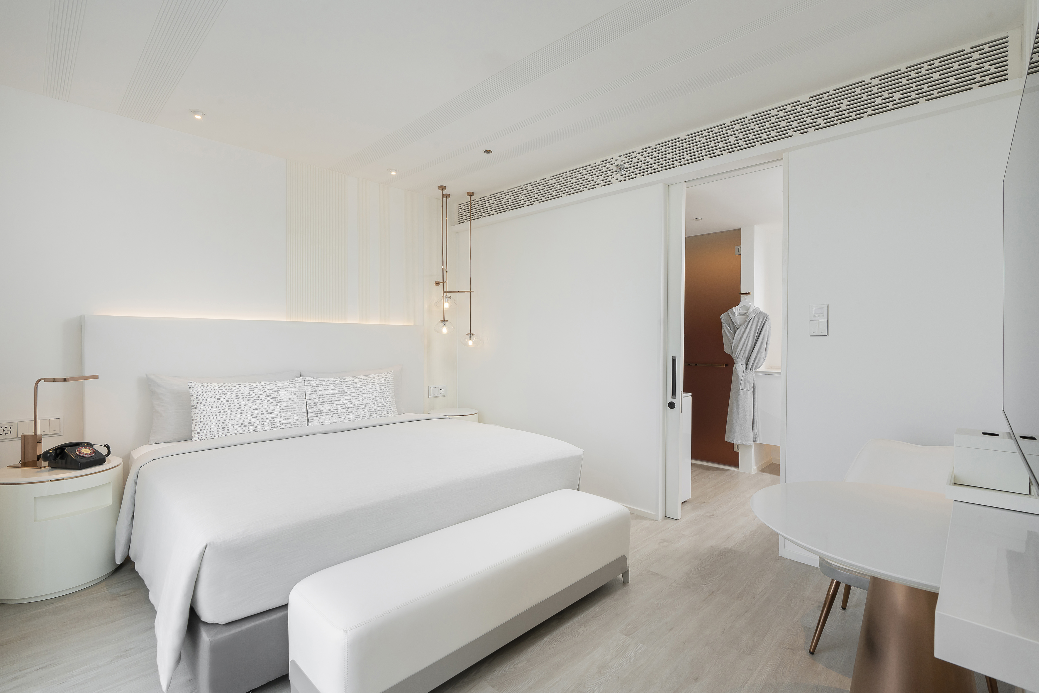Modern white hotel bedroom with king bed, minimalist design, and copper accents.