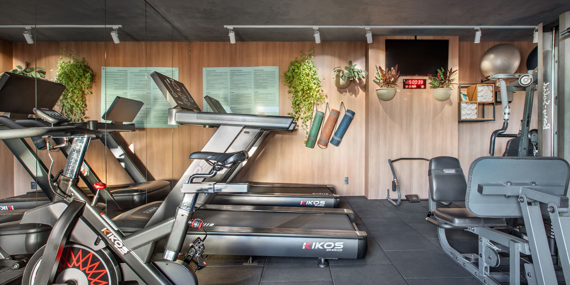 Modern gym with KIKOS treadmills, exercise bikes, weight machines, wood walls.