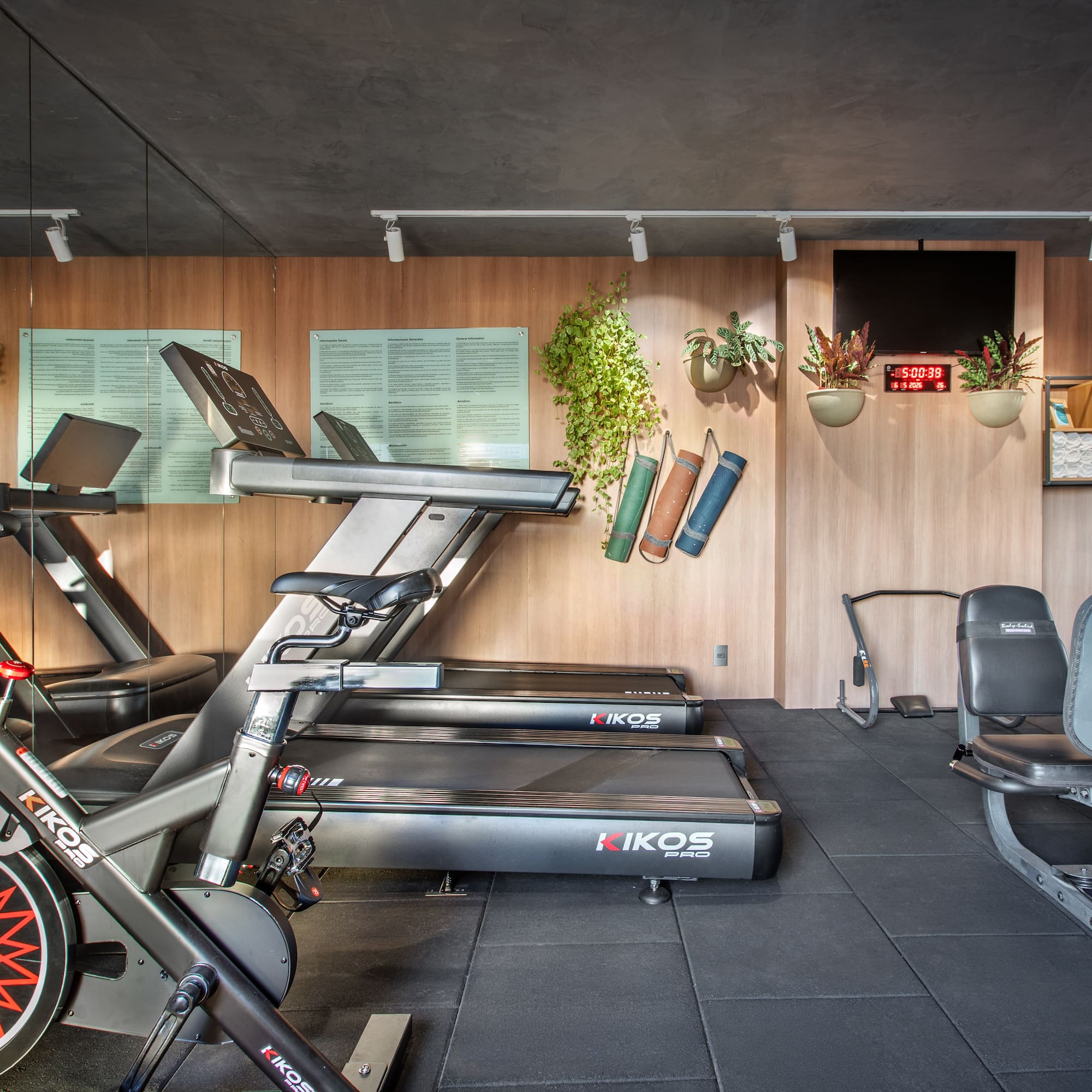 Modern gym with KIKOS treadmills, exercise bikes, weight machines, wood walls.