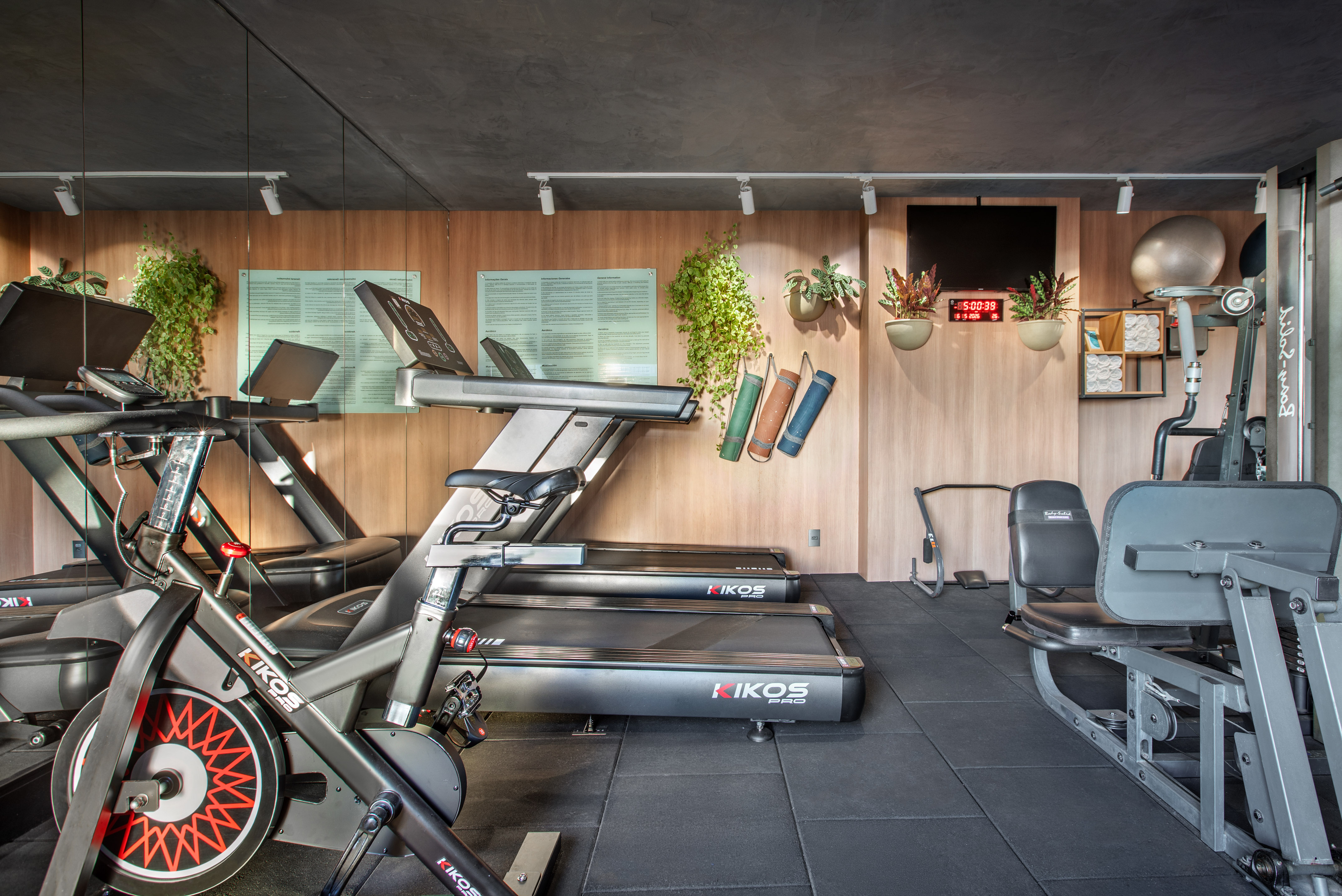 Modern gym with KIKOS treadmills, exercise bikes, weight machines, wood walls.