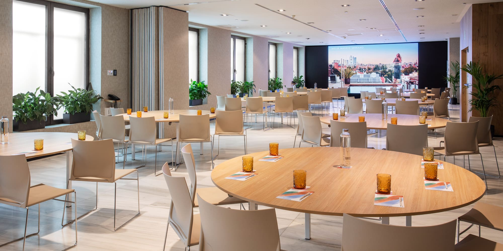 Sleek conference room with round tables, beige chairs, windows, and large screen