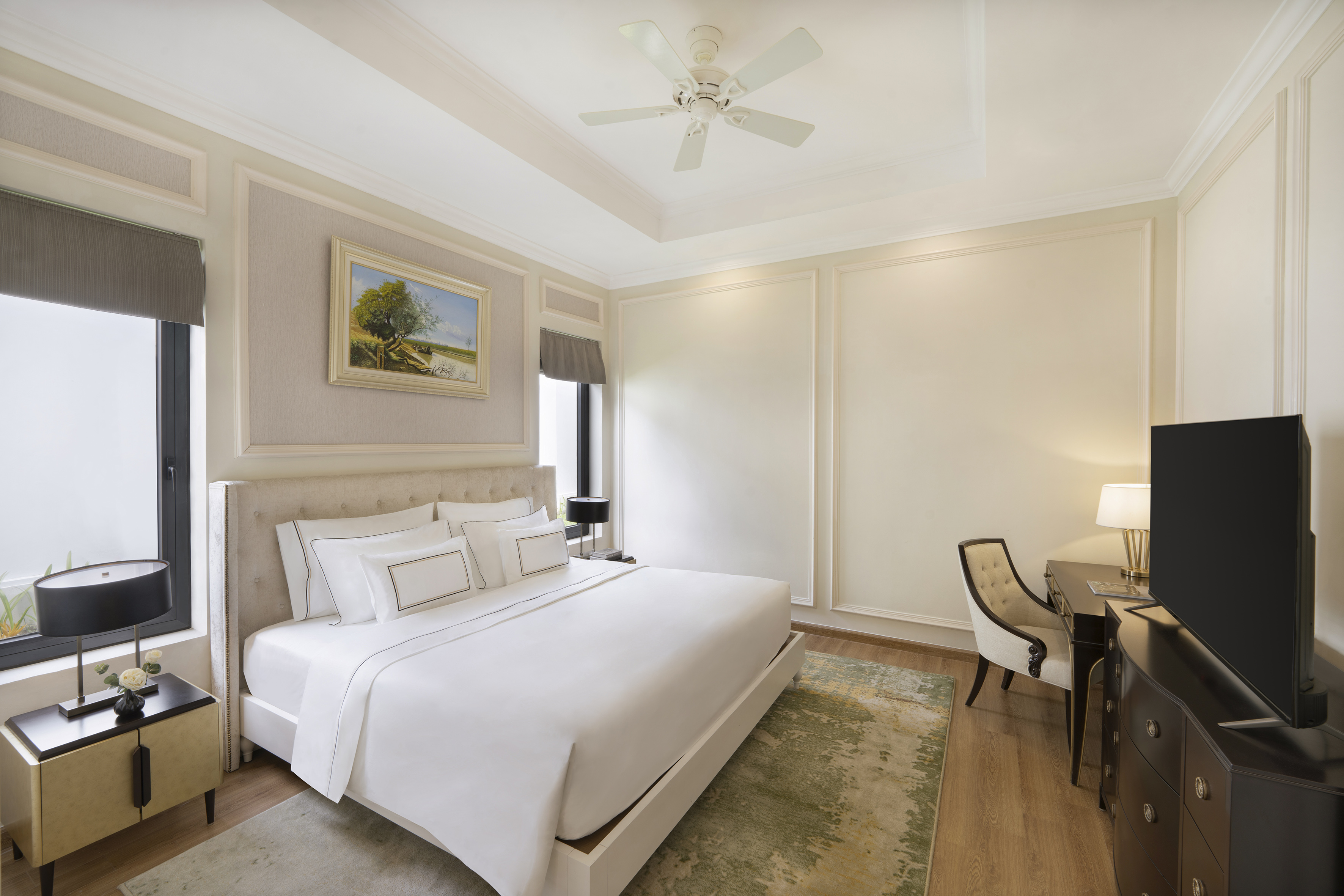 Elegant hotel bedroom with king bed, white linens, desk, TV, and ceiling fan.