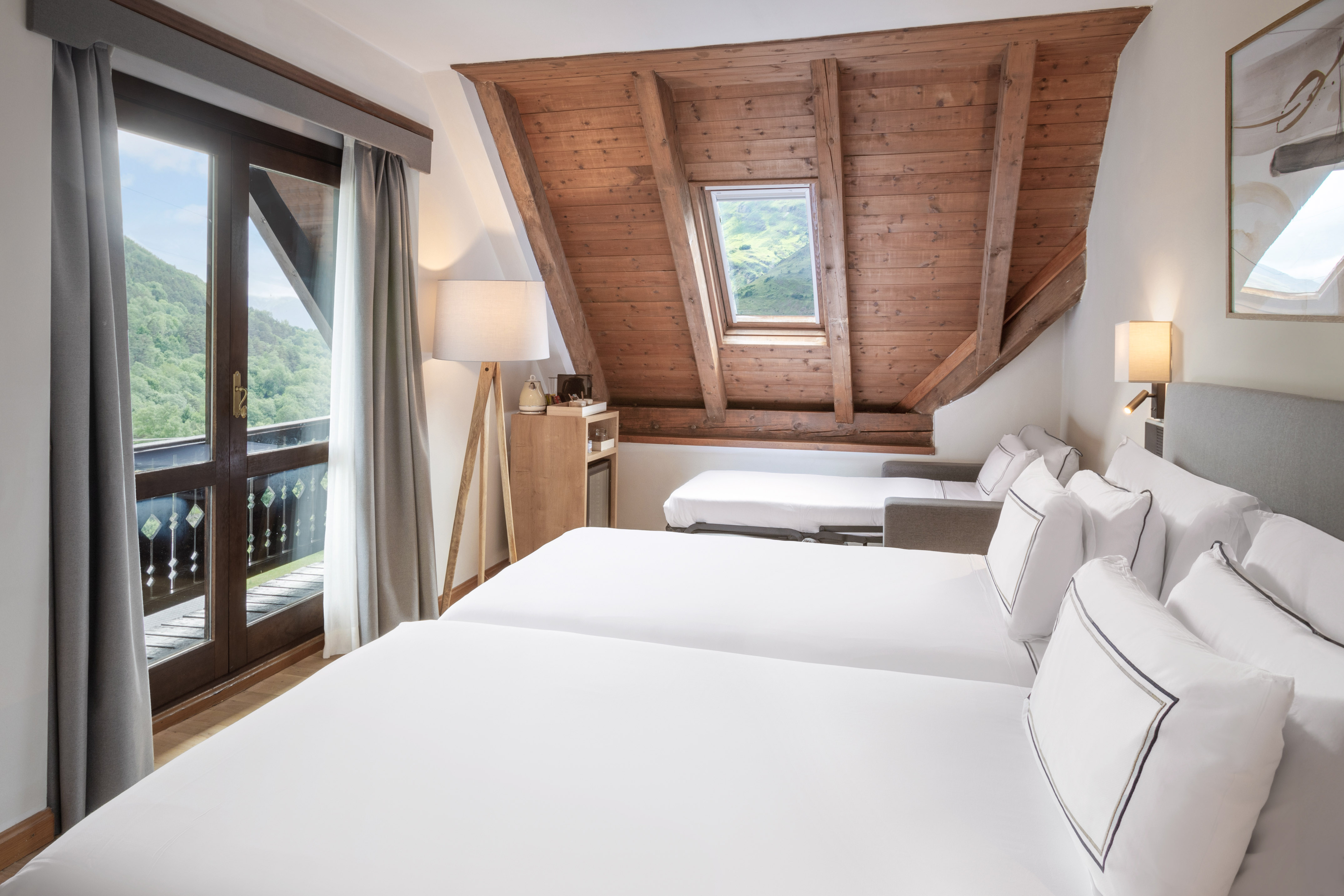 Hotel room with twin beds, mountain view balcony, and wooden attic skylight.