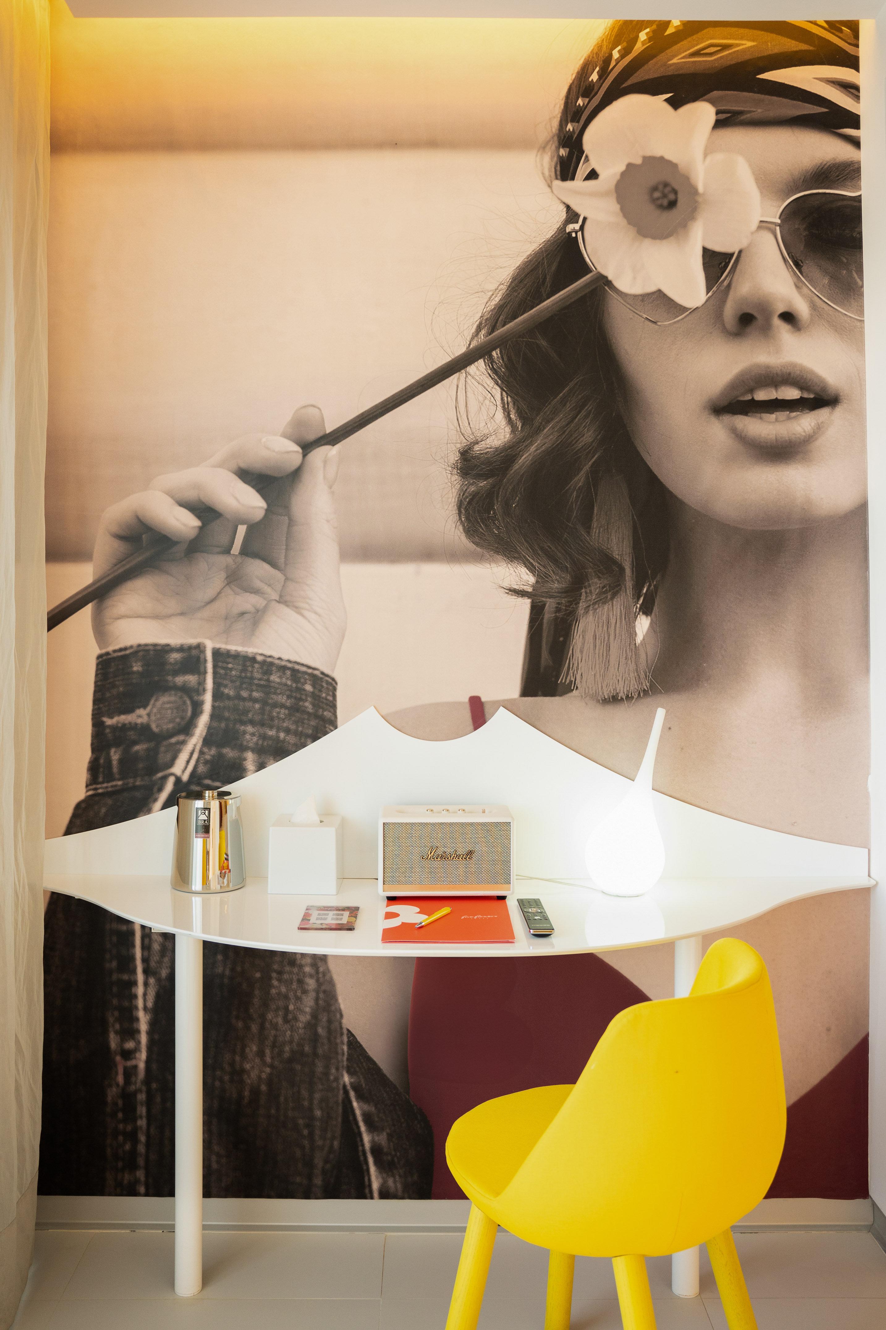 Stylish hotel desk with woman mural, yellow chair, Marshall speaker.