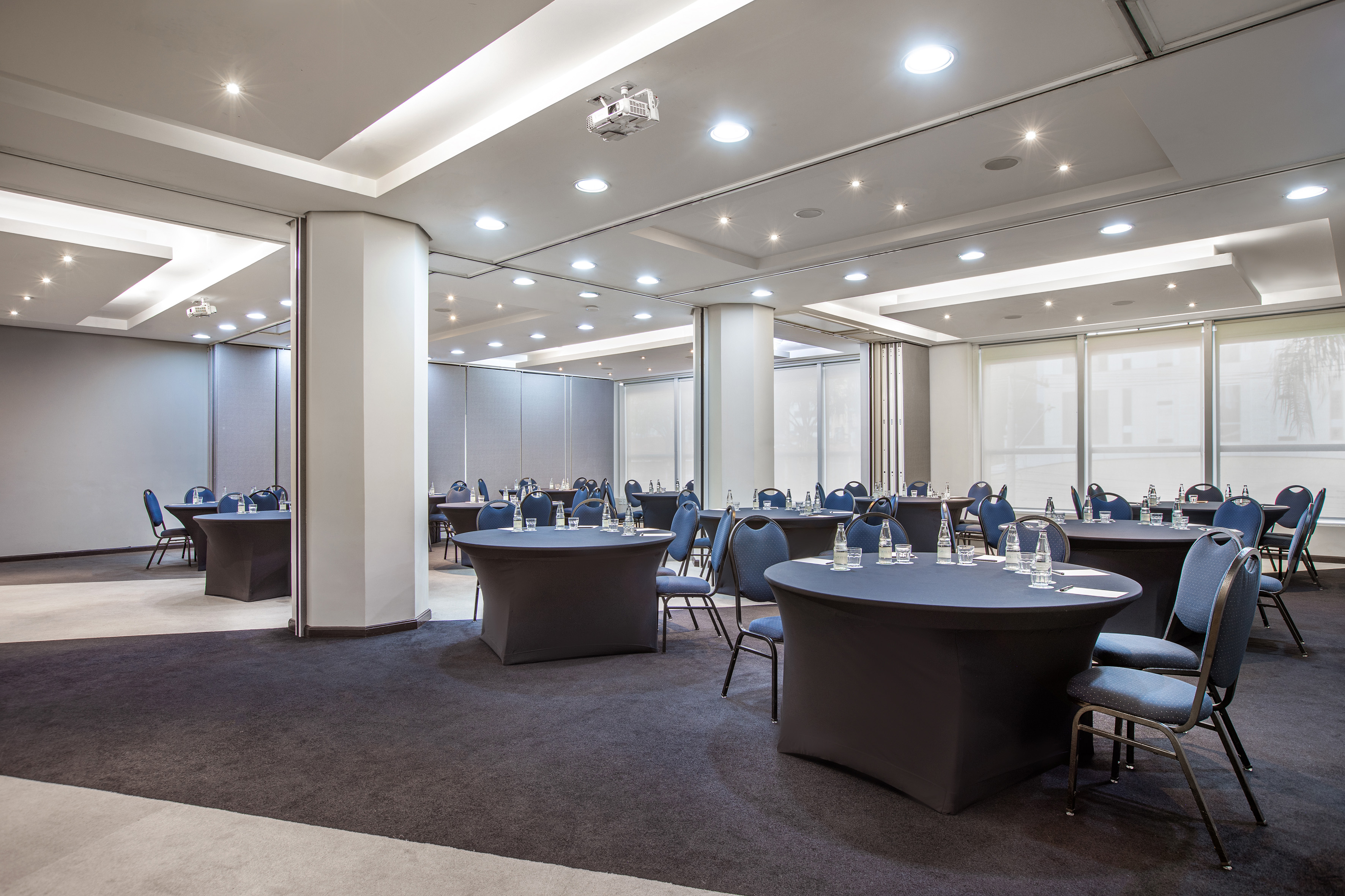 Modern conference room with blue chairs, round tables, and ceiling projector setup.