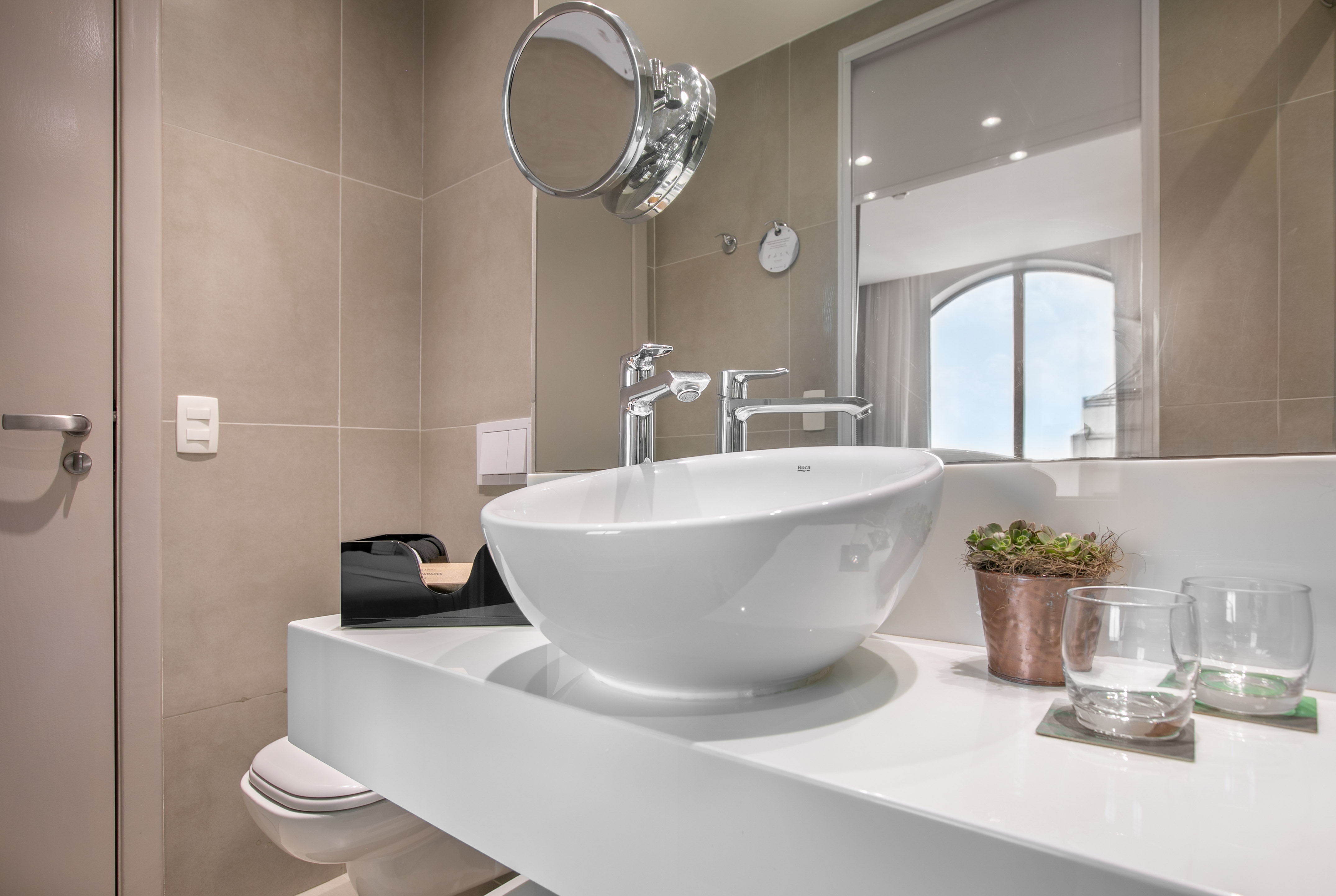 Modern bathroom vanity with white bowl sink, chrome faucets, and wall mirror.