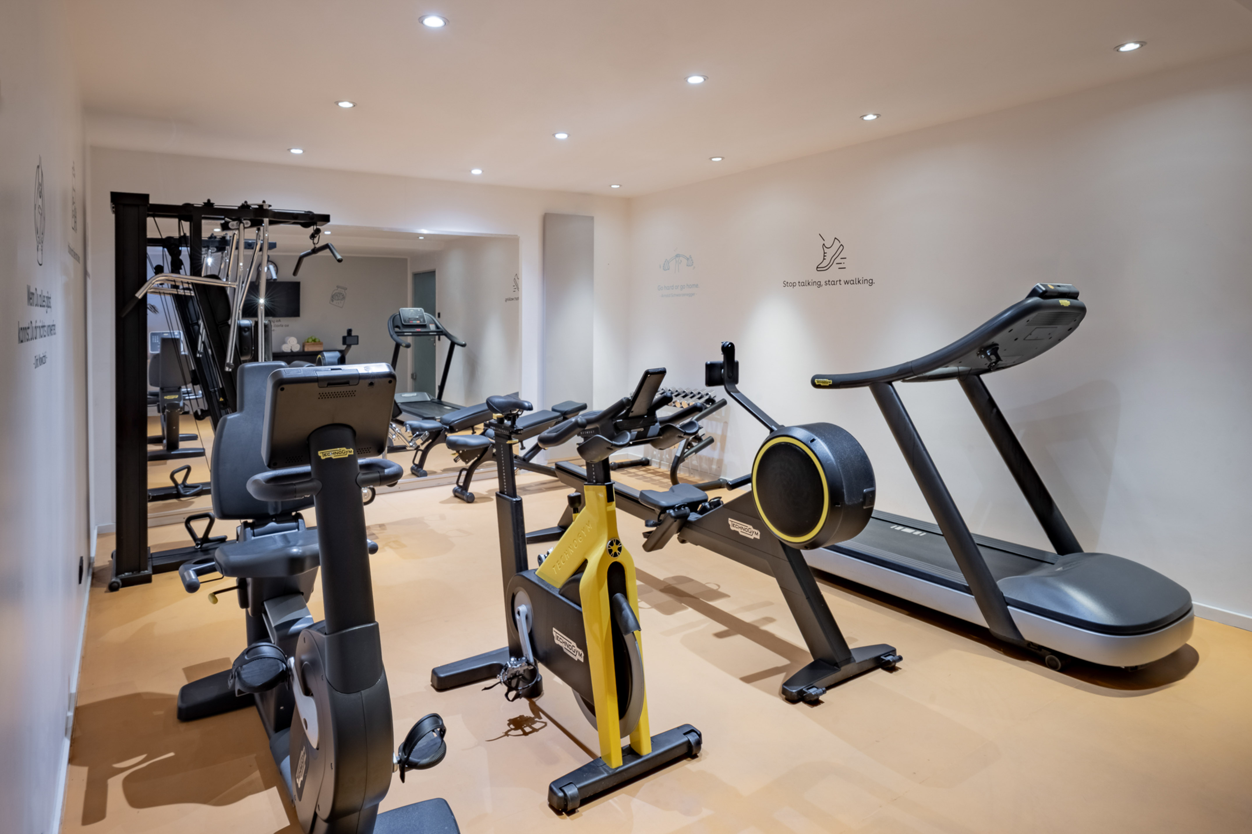 Modern Technogym fitness room with treadmill, exercise bikes, and weight equipment.
