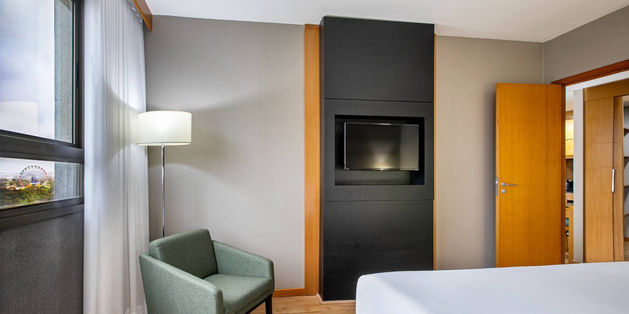 Hotel room with bed, armchair, TV, and window view of a Ferris wheel.
