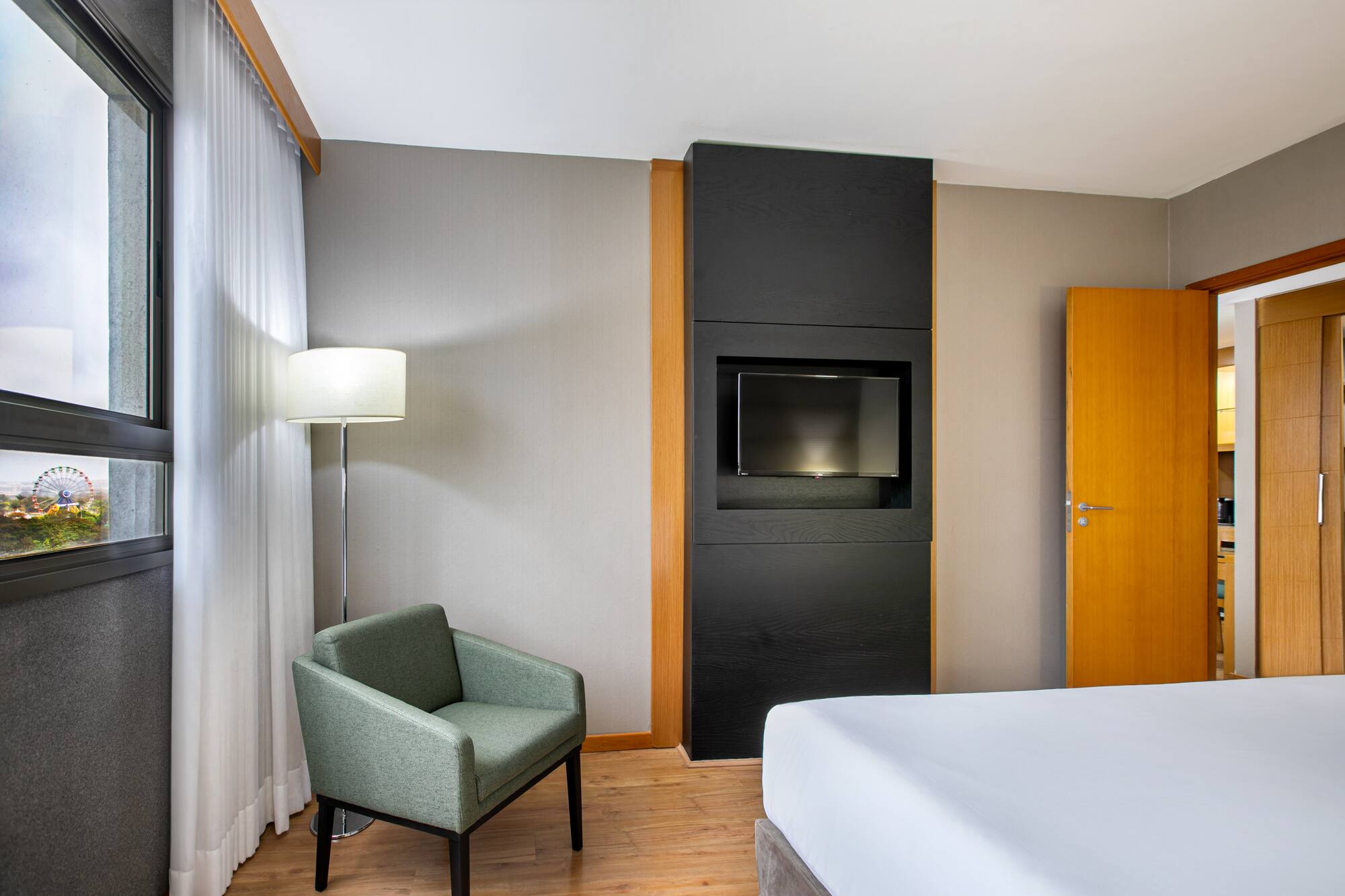 Hotel room with bed, armchair, TV, and window view of a Ferris wheel.