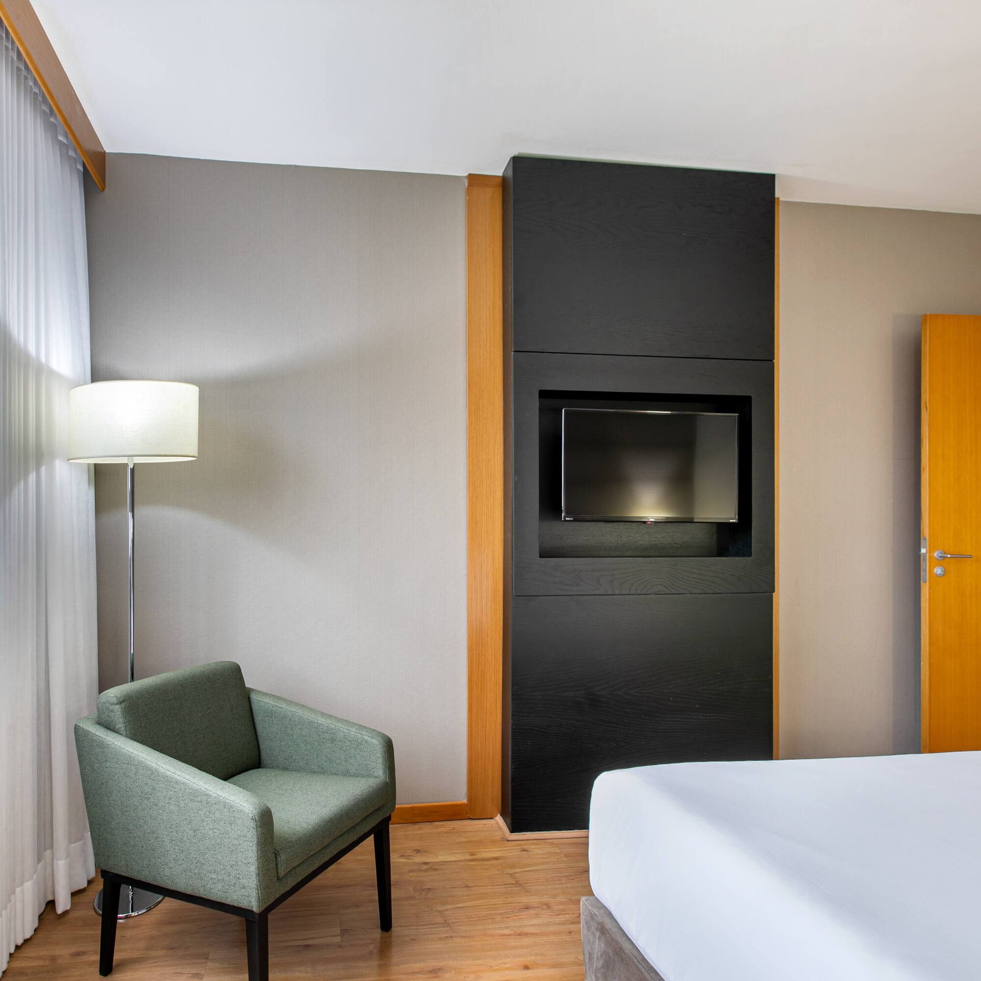 Hotel room with bed, armchair, TV, and window view of a Ferris wheel.