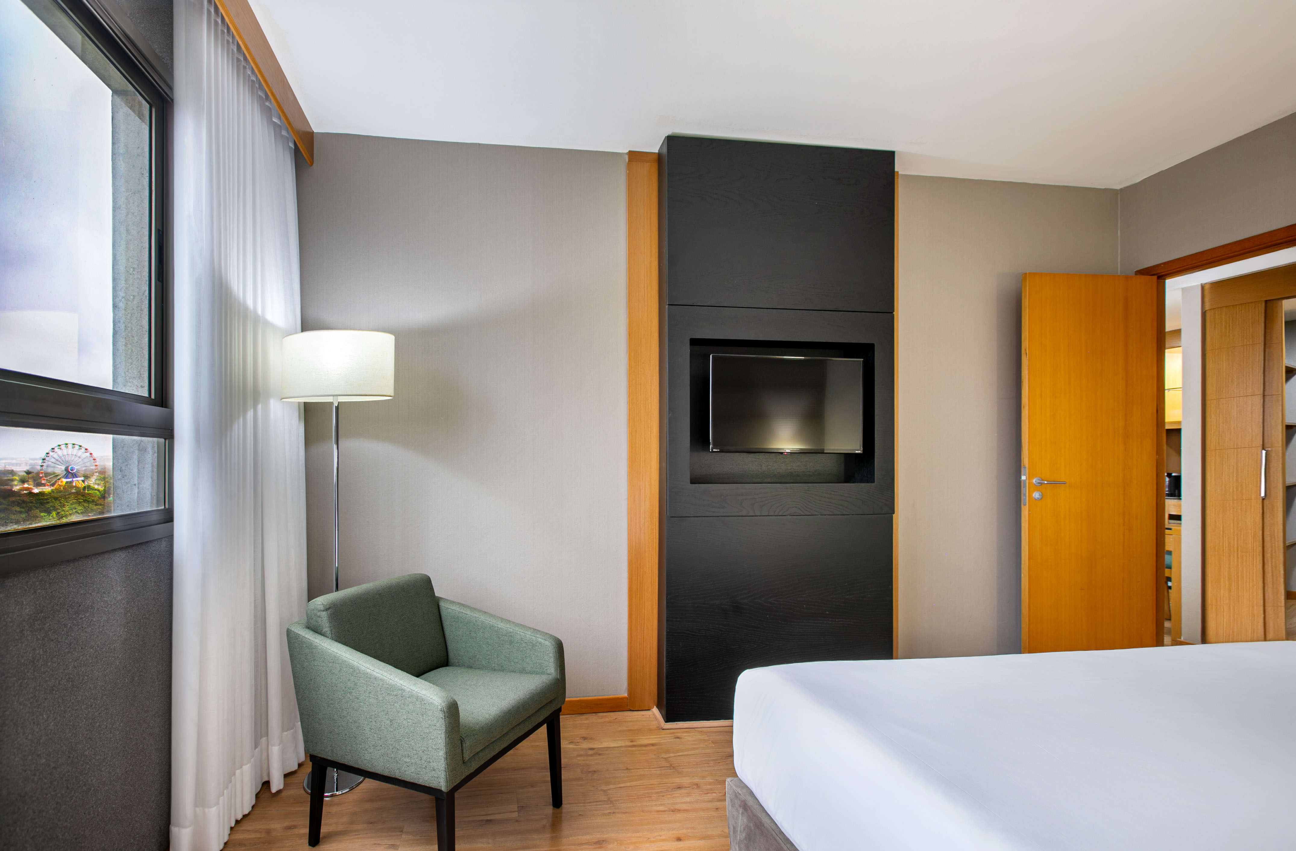 Hotel room with bed, armchair, TV, and window view of a Ferris wheel.