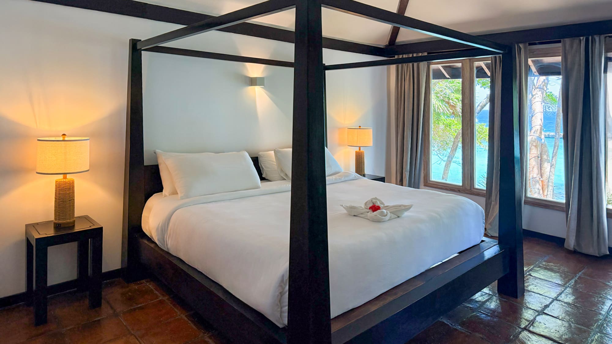 Tropical bedroom with dark four-poster bed, white linens, ocean view.
