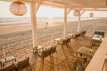 Beachfront terrace with outdoor seating, ocean view, and sunset glow.