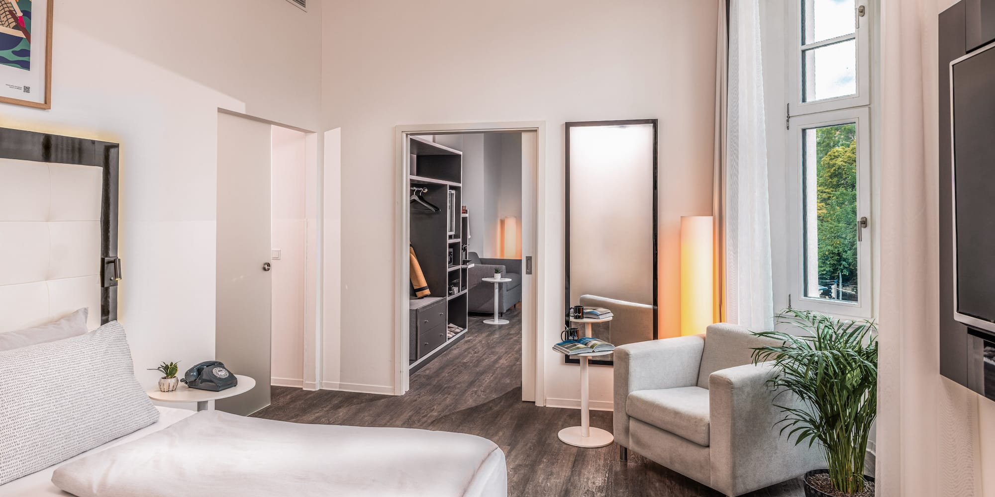 Modern hotel bedroom with bed, armchair, window, and walk-in closet.