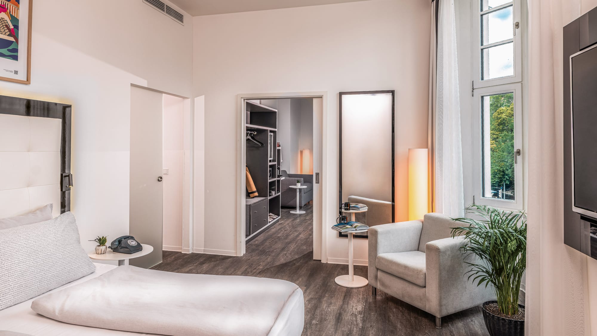 Modern hotel bedroom with bed, armchair, window, and walk-in closet.