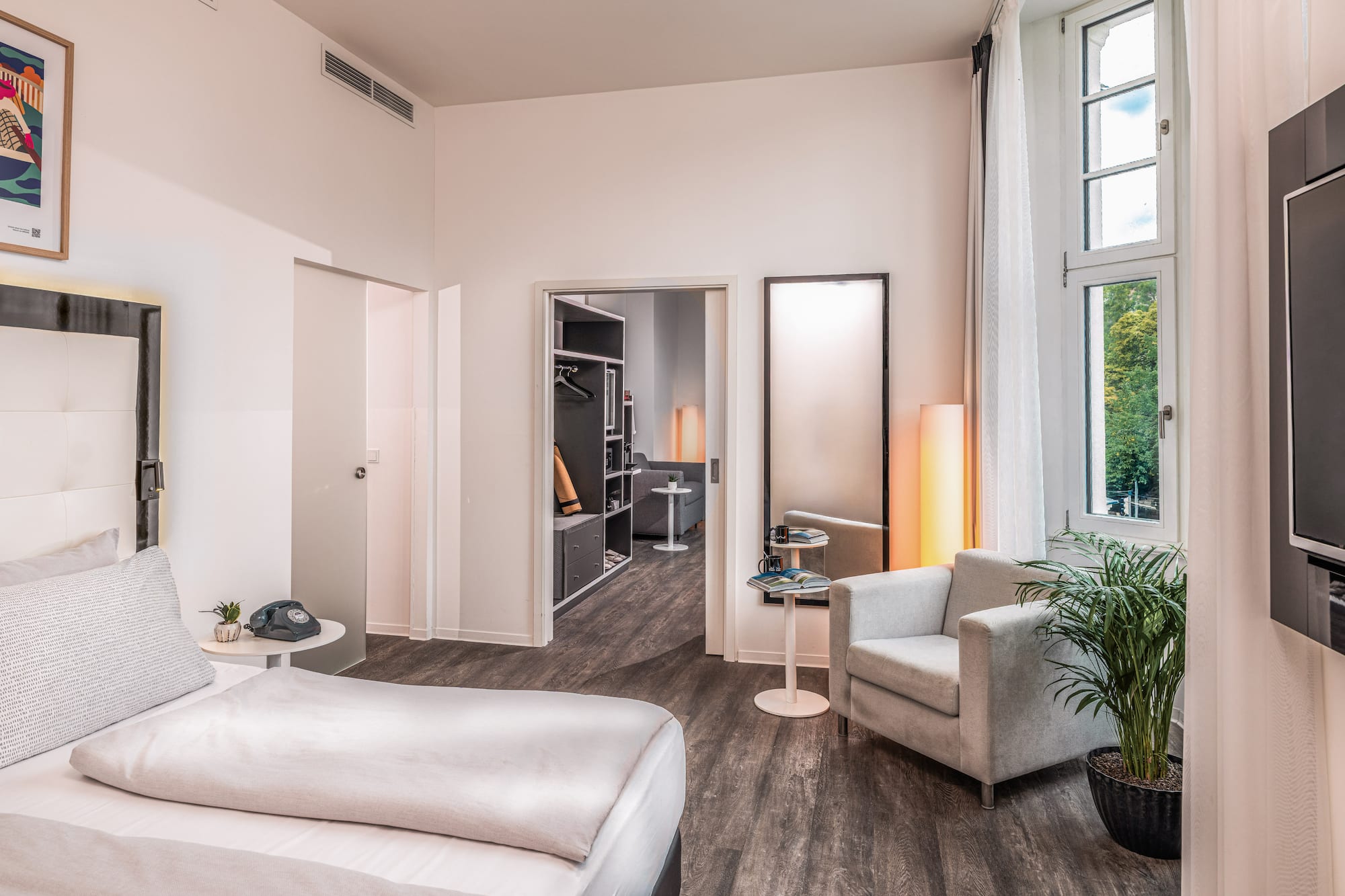 Modern hotel bedroom with bed, armchair, window, and walk-in closet.
