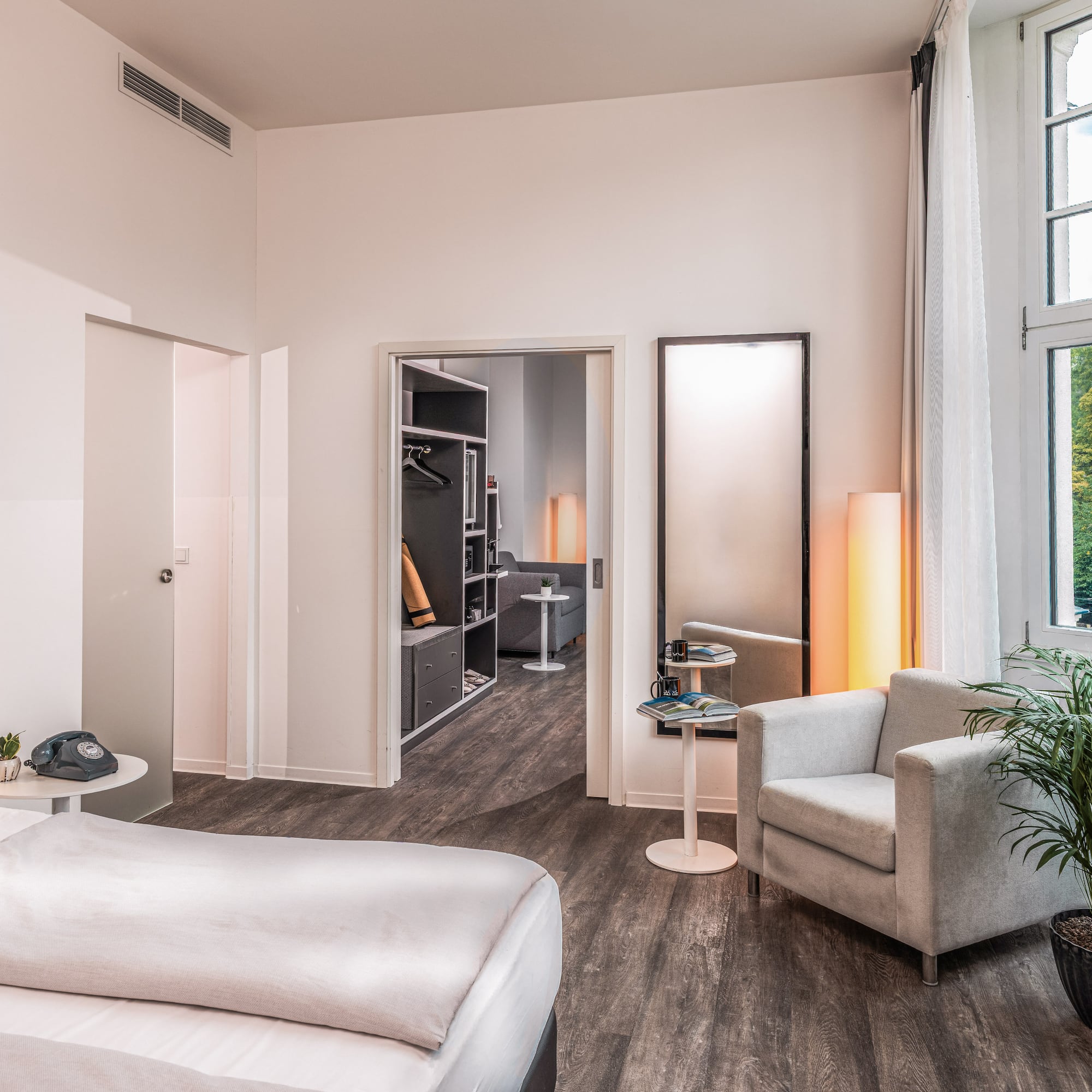 Modern hotel bedroom with bed, armchair, window, and walk-in closet.