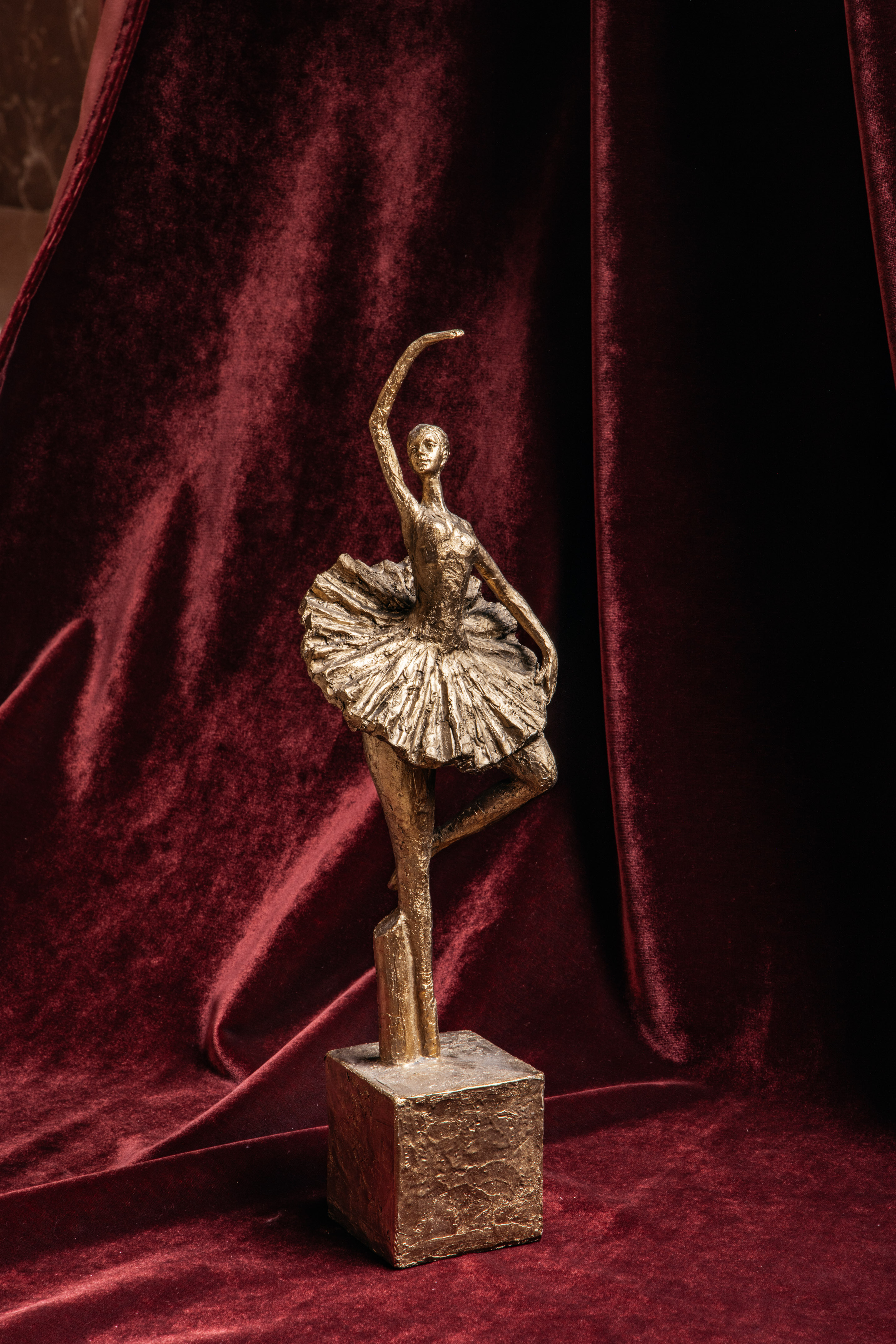A ballerina statue set against a red velvet backdrop.