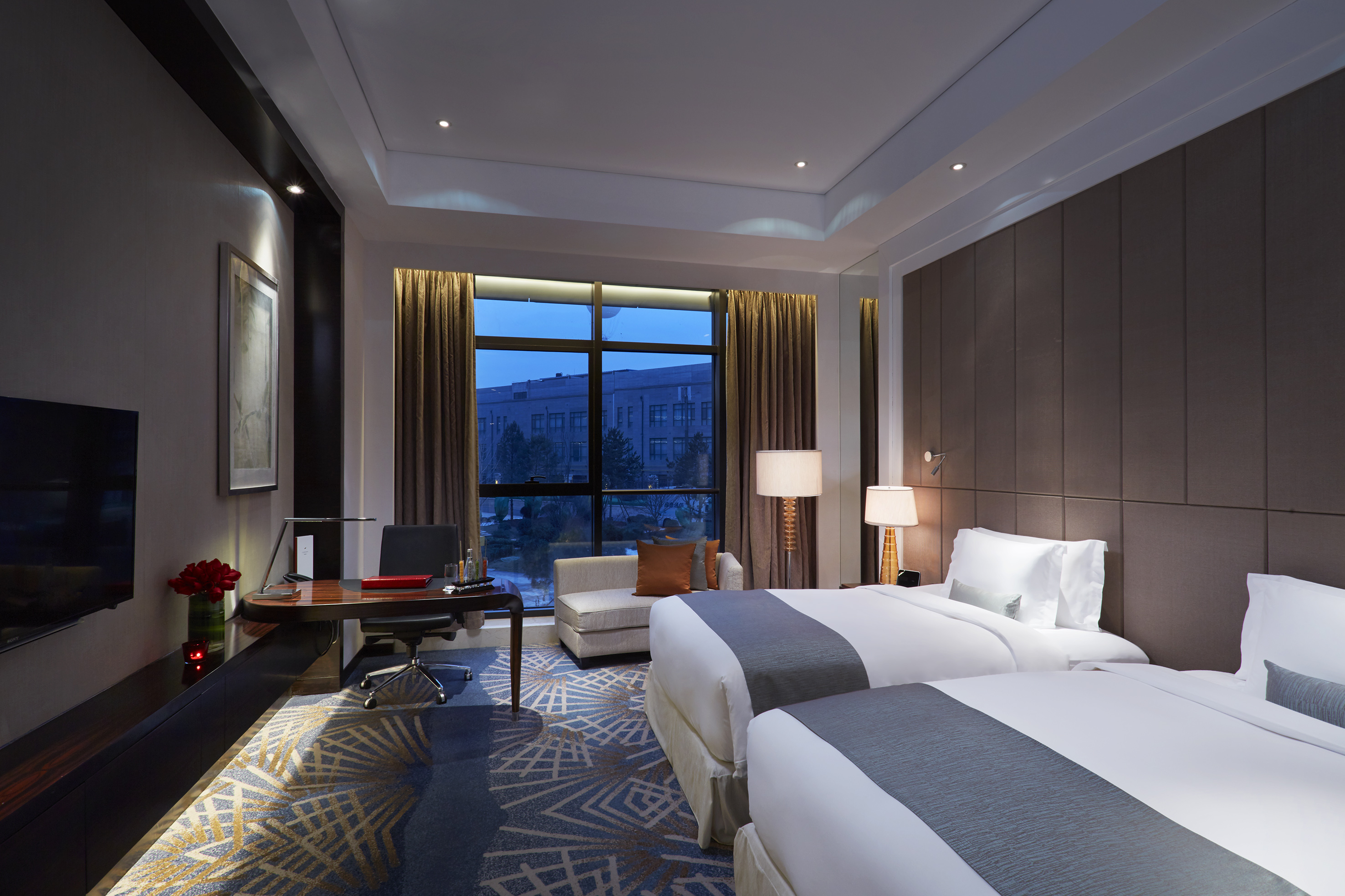 Luxury hotel room with two beds, work desk, and night view.