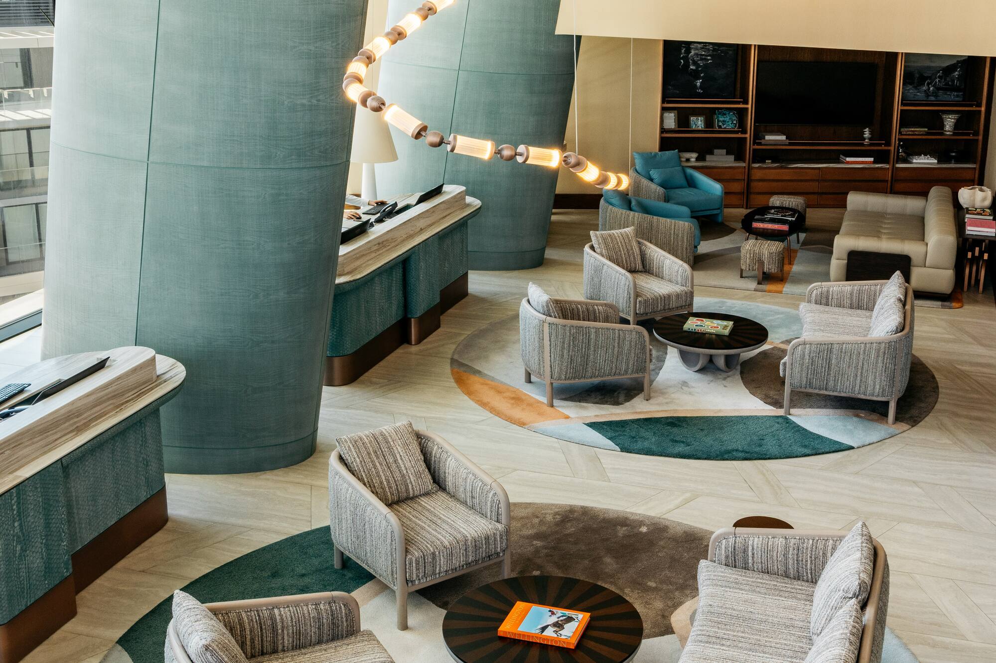 Modern hotel lobby with spiral chandelier, sleek seating, and abstract rugs.