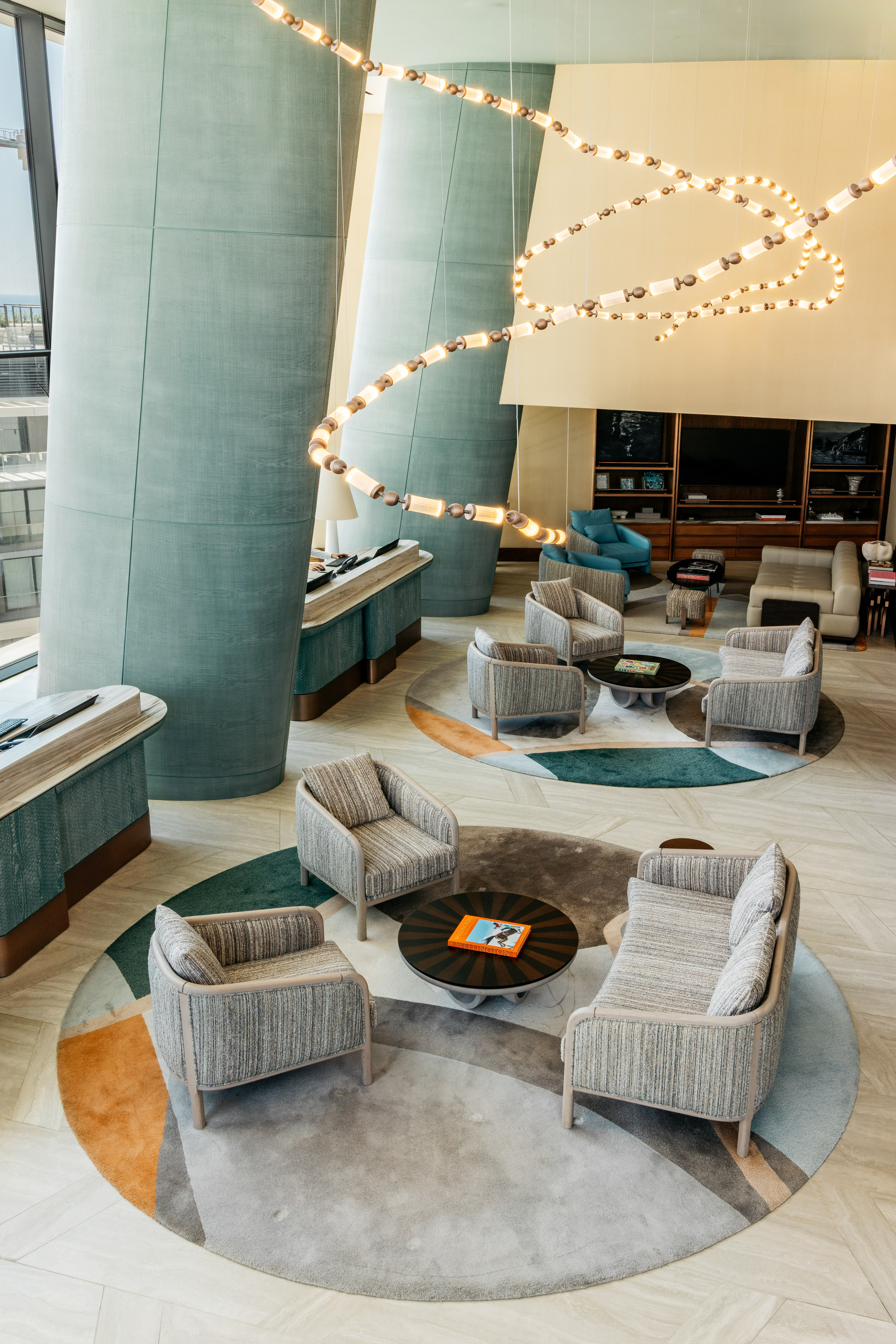 Modern hotel lobby with spiral chandelier, sleek seating, and abstract rugs.
