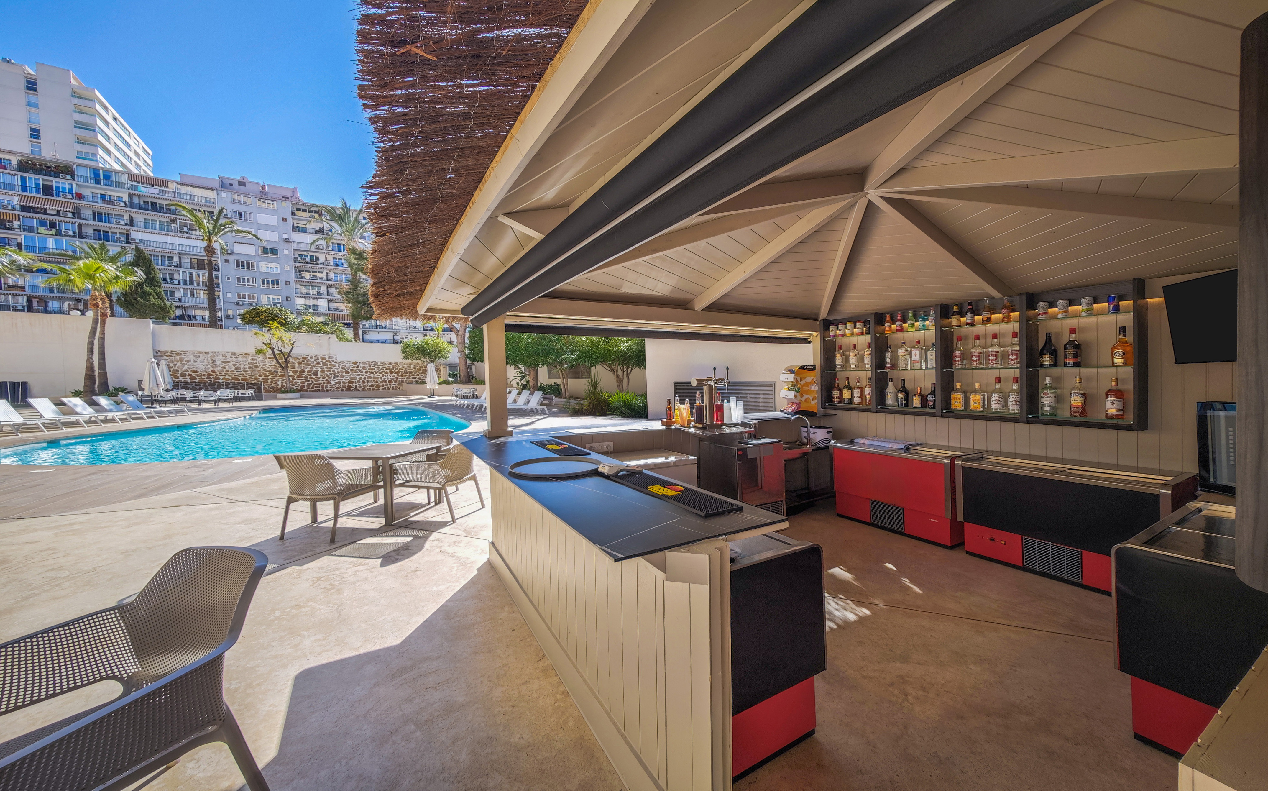 Sunny outdoor pool bar with liquor display, counter, and hotel swimming pool.
