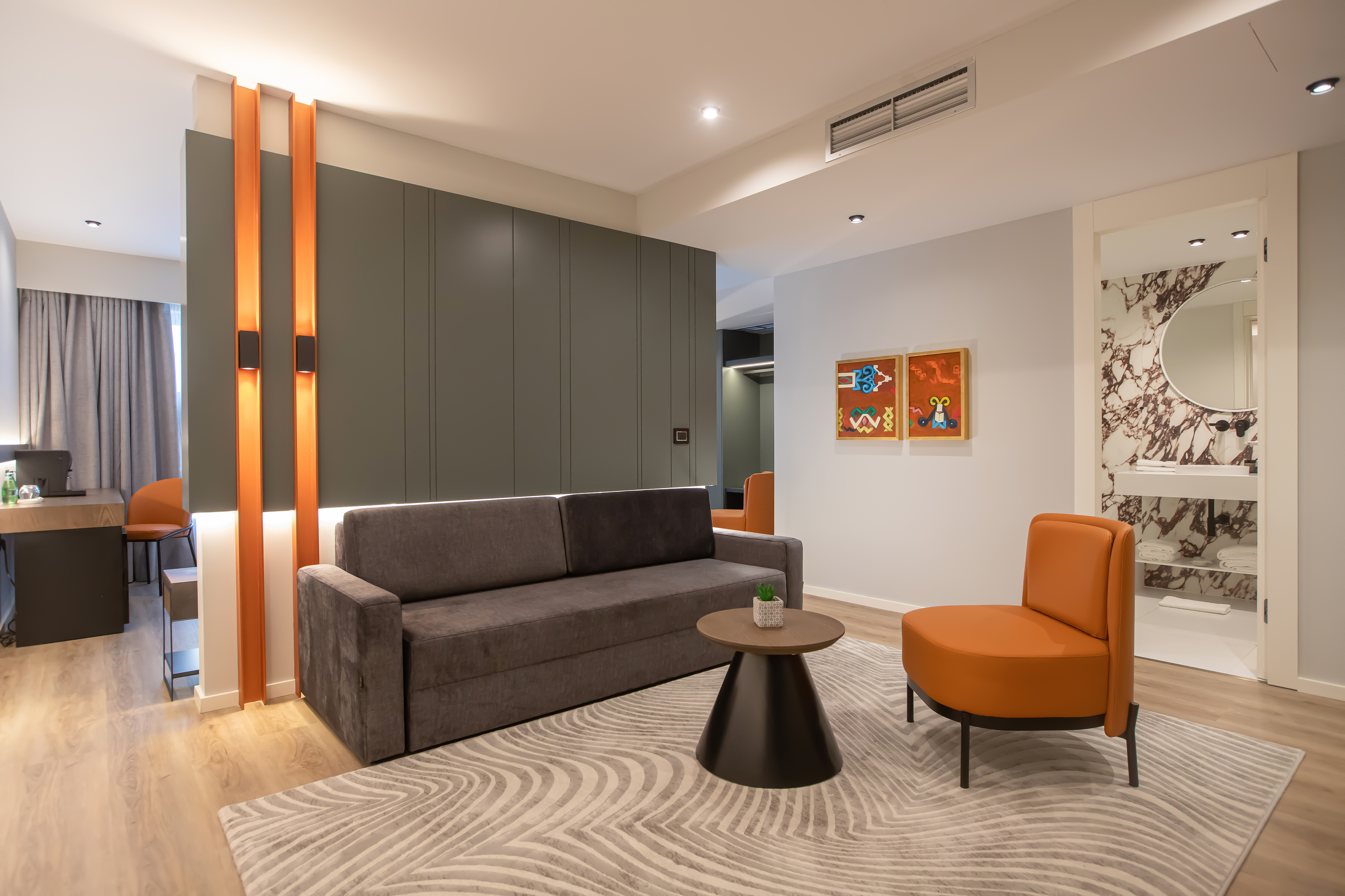 Modern hotel suite living area with grey sofa, orange chair, and stylish lighting.