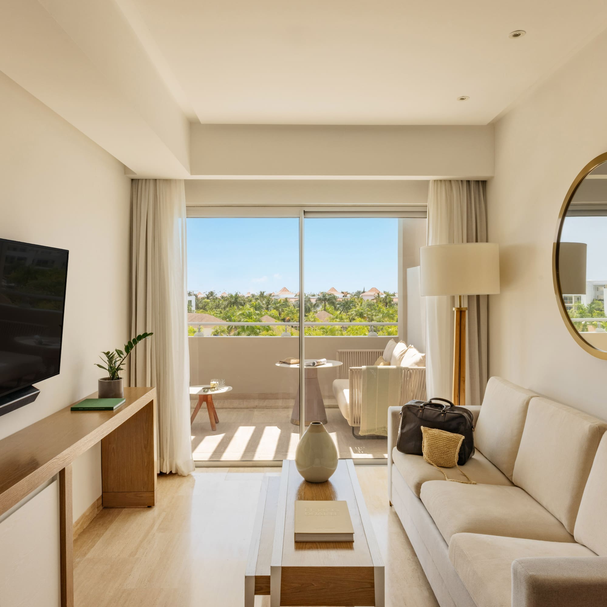 Modern hotel suite living room with private balcony and tropical resort view.