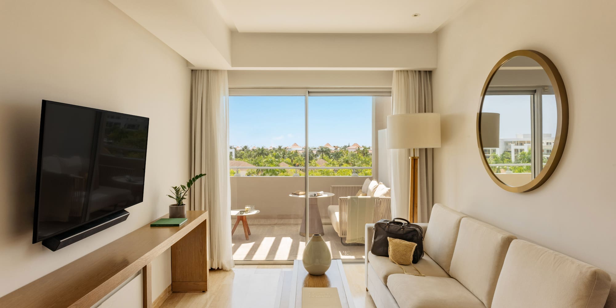 Bright resort suite living room with sofa, balcony, and tropical views.