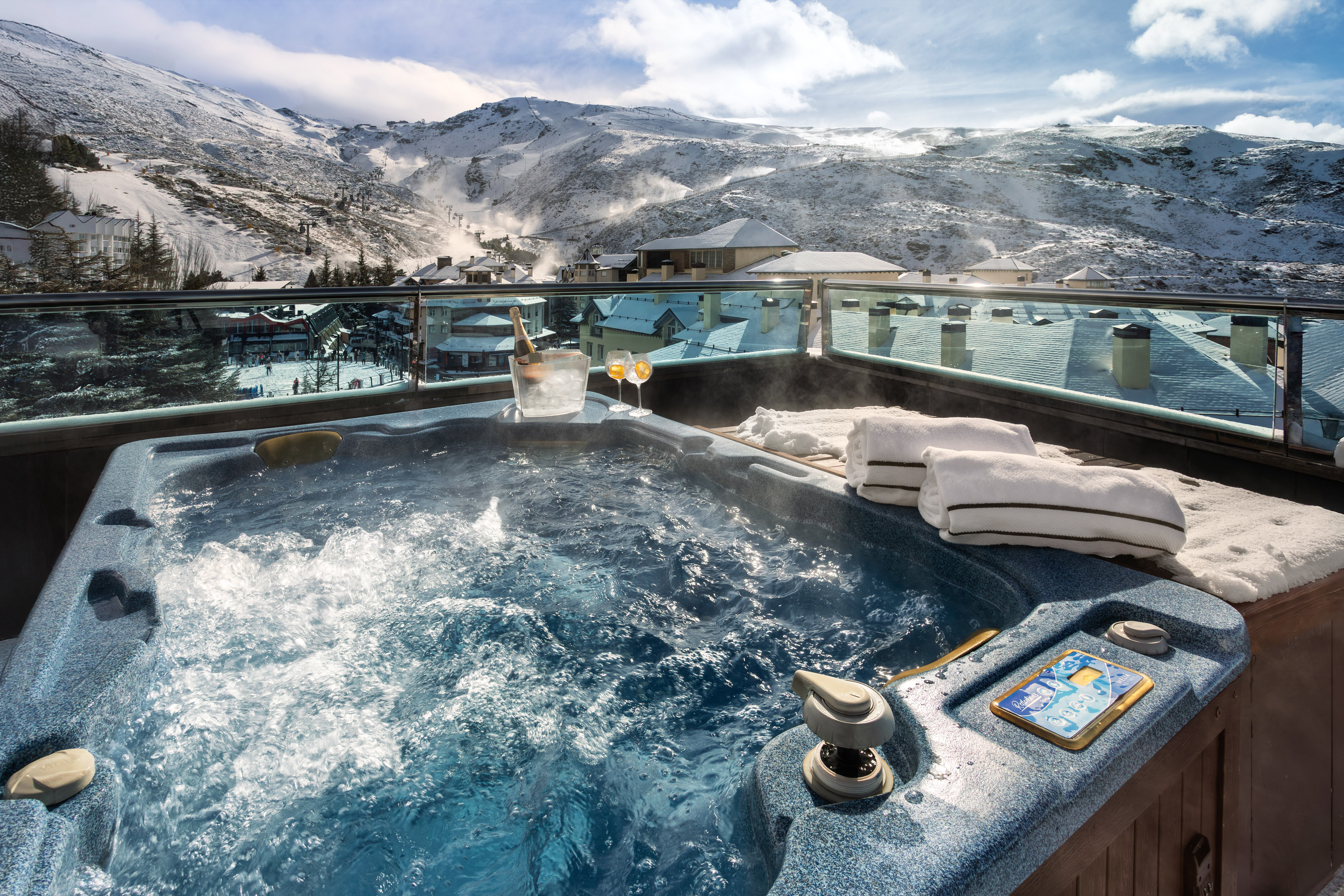 Hot tub with champagne on balcony, snowy mountain ski resort view.