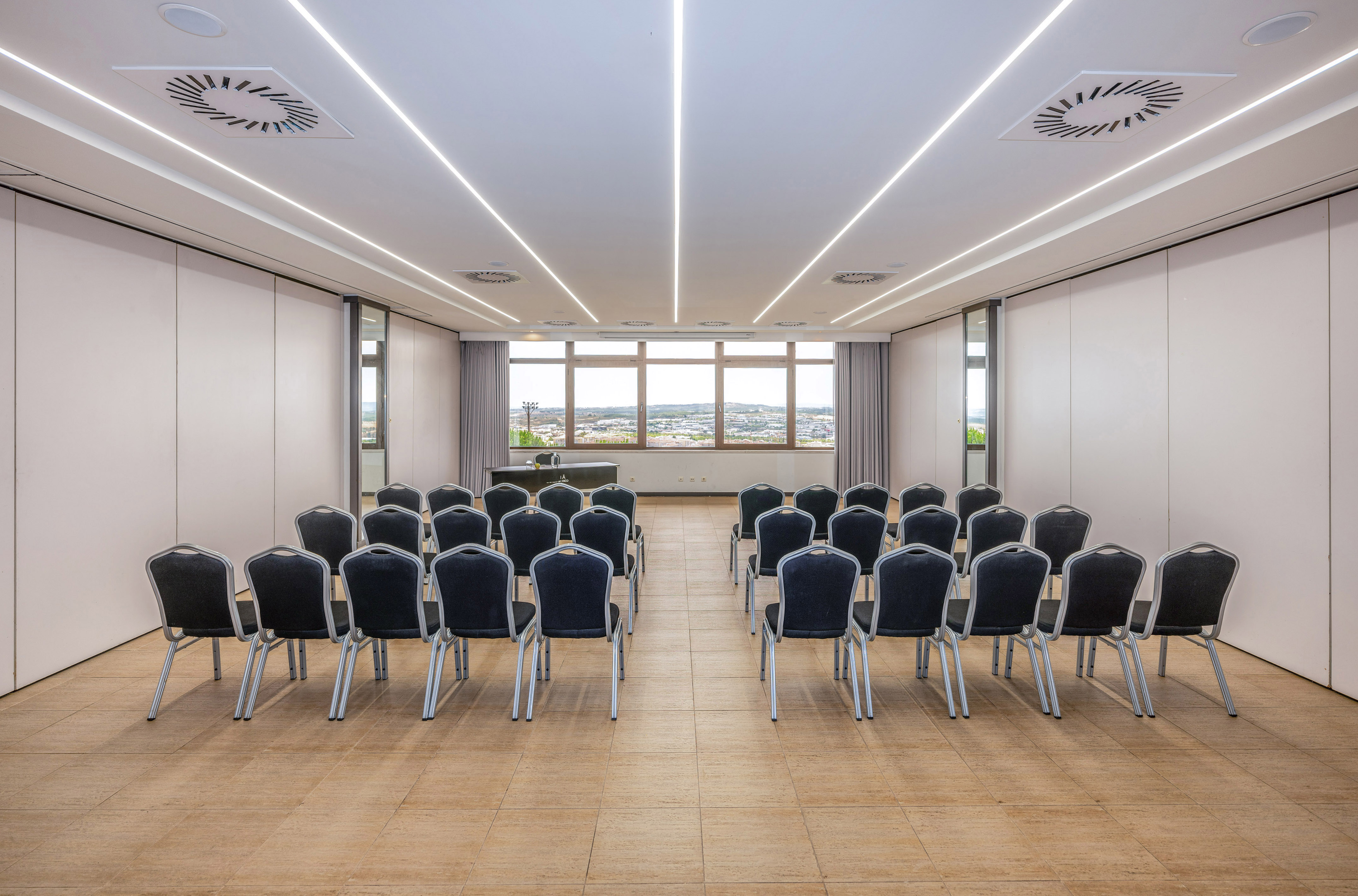 Modern conference room with theater seating, bright lighting, and city view windows.