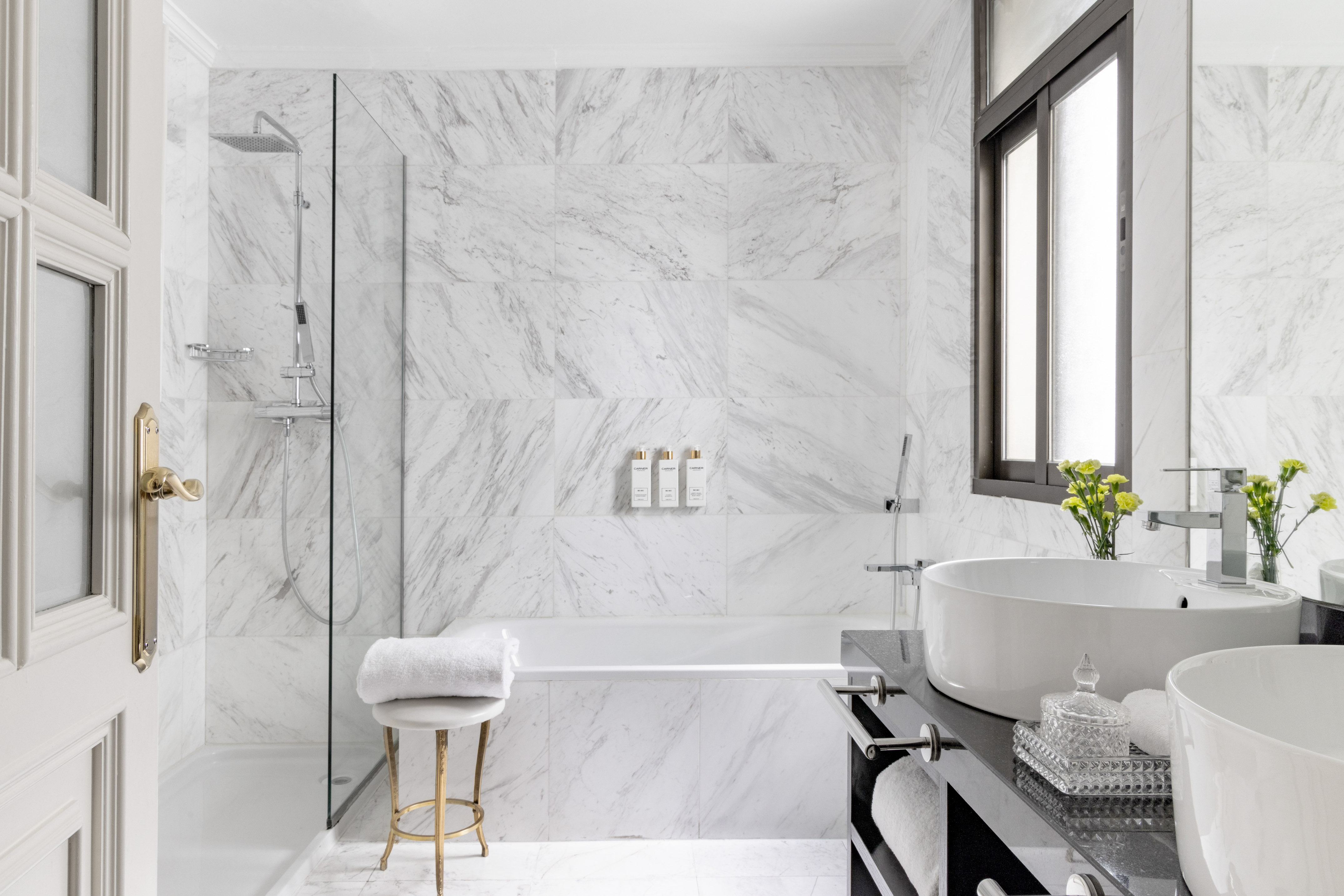 Luxury marble bathroom with glass shower, built-in tub, and dual vessel sinks.