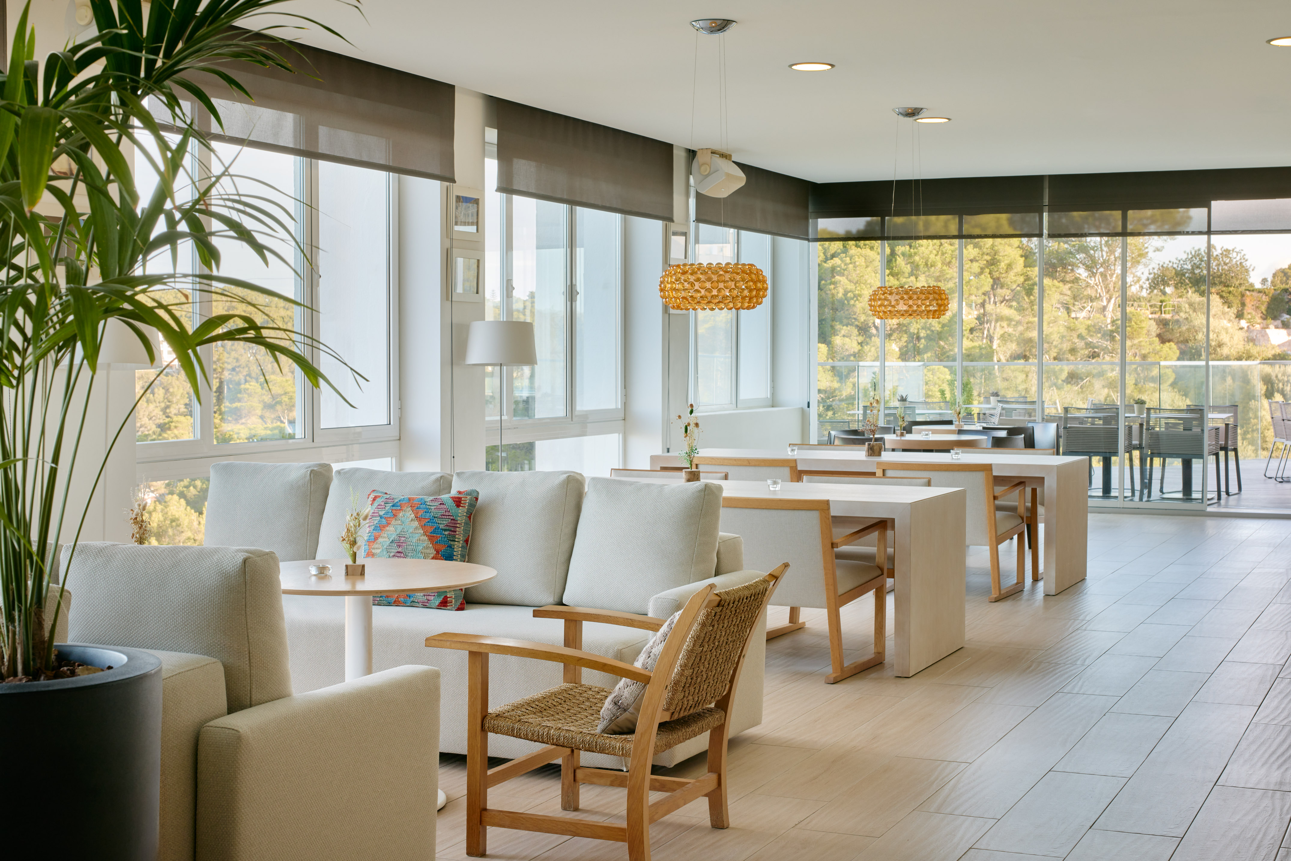 Bright modern hotel lounge with panoramic windows, sofas, and dining tables.
