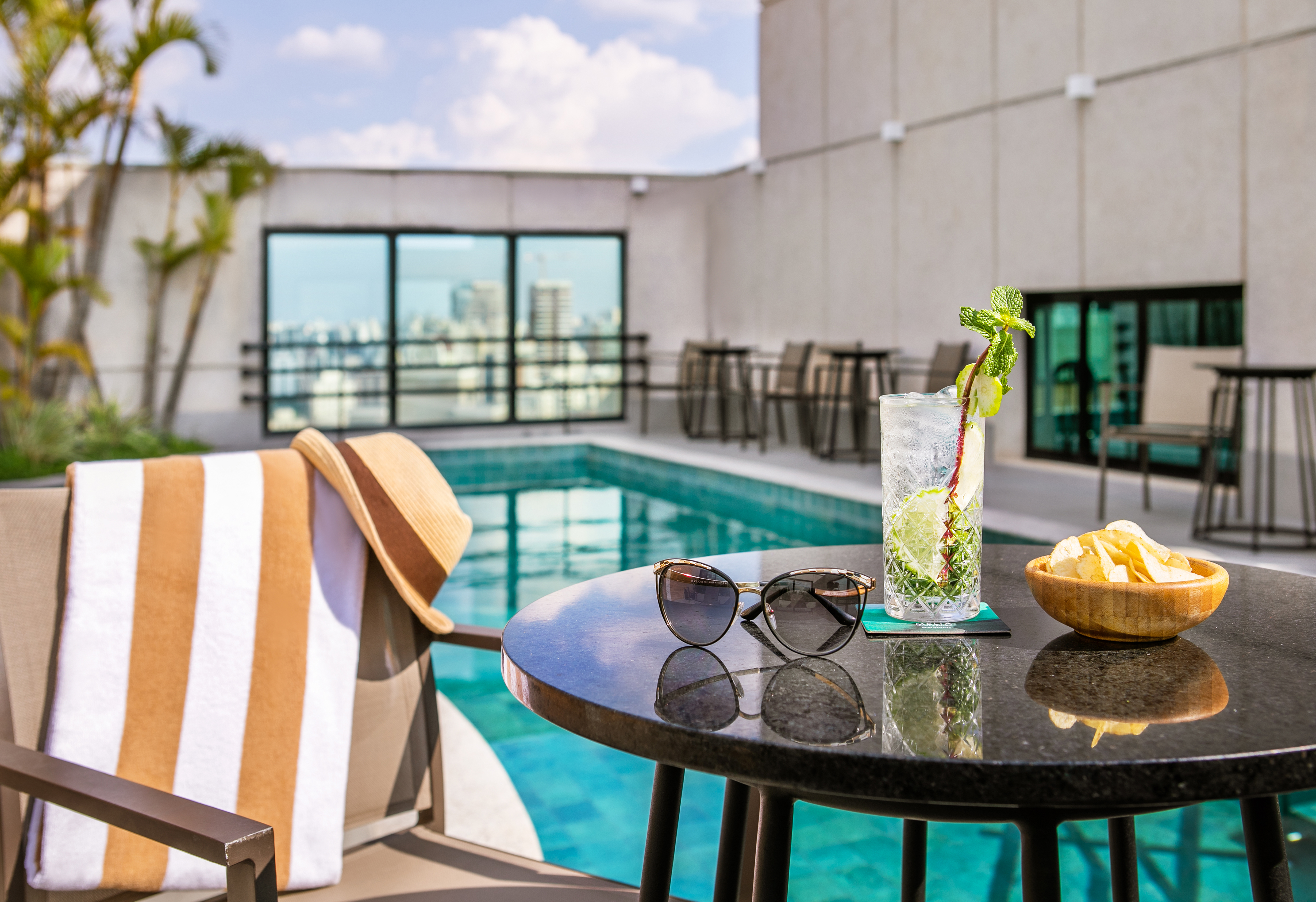 Rooftop pool lounge with a cocktail, chips, sunglasses, and towel.