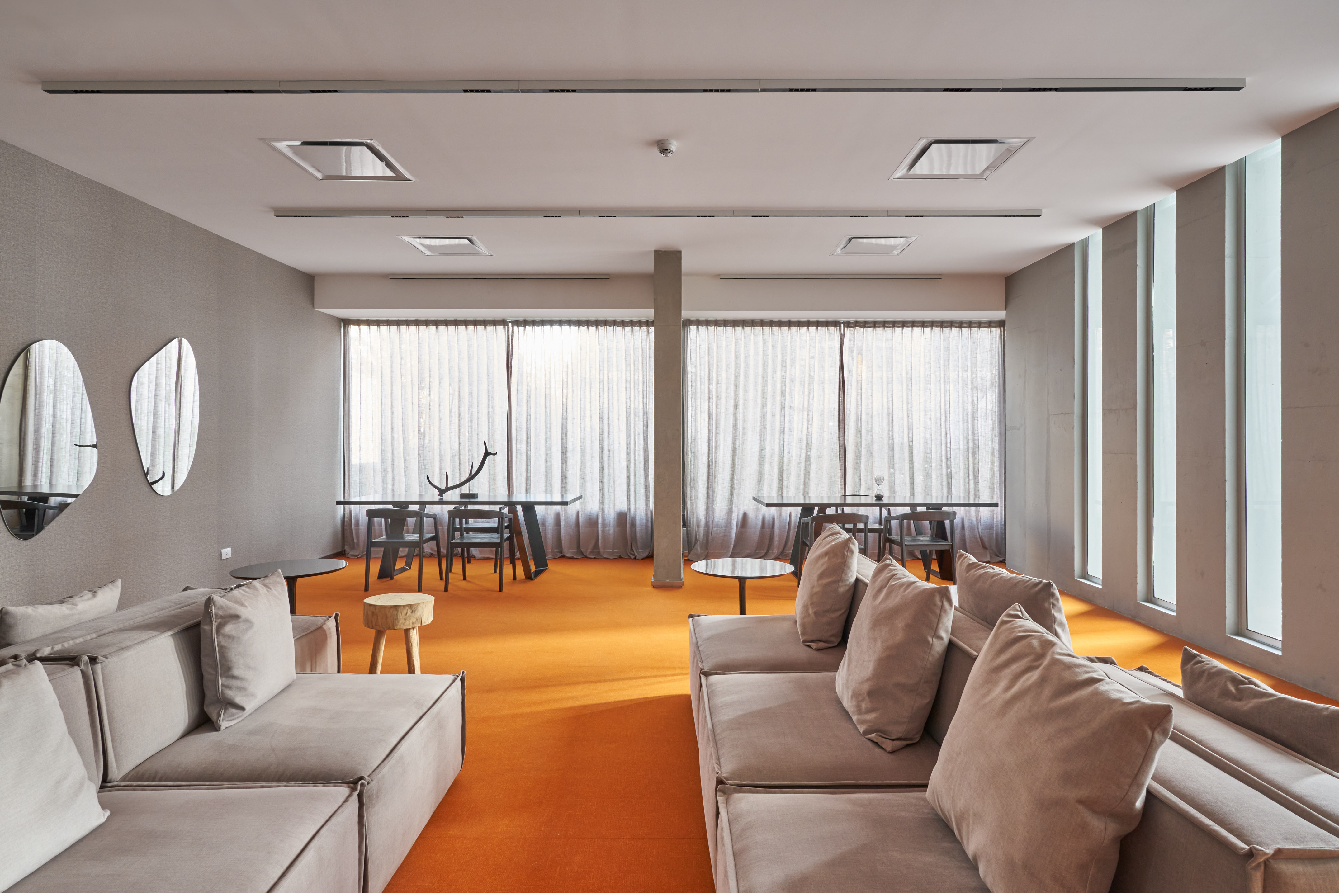 Modern lounge interior with orange carpet, grey sofas, and large windows.