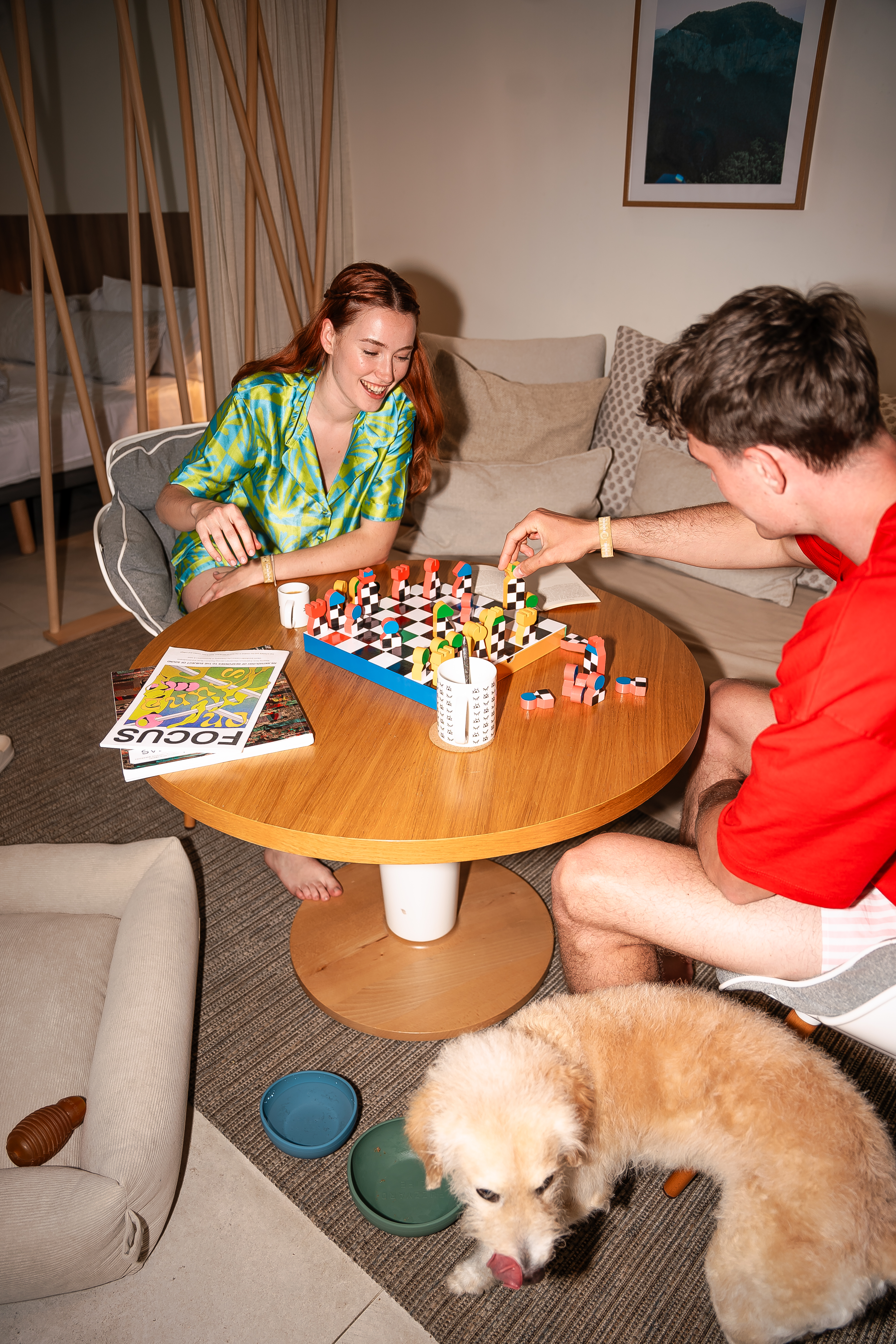 Couple smiling, playing colorful board game indoors, small dog resting.
