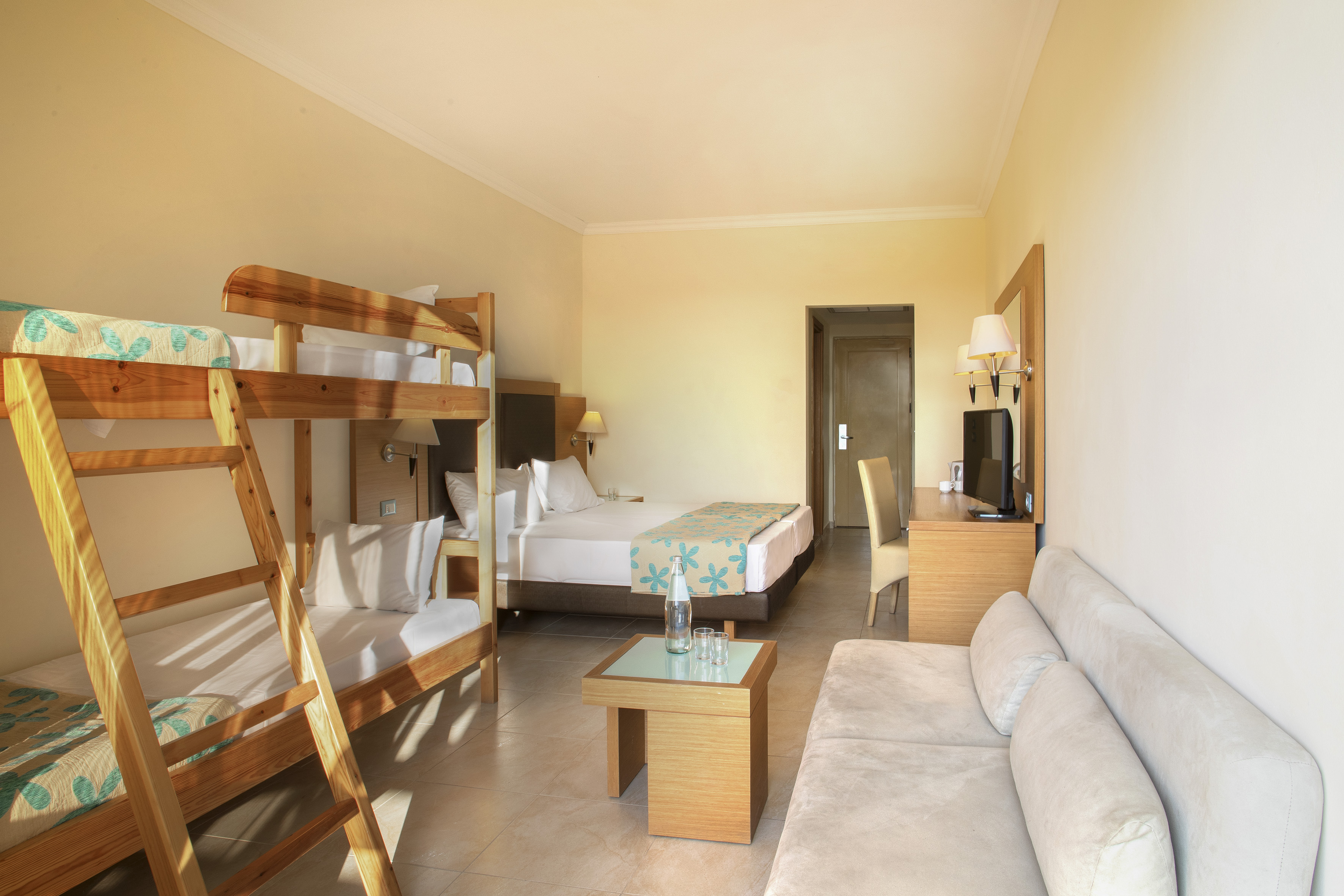Spacious hotel family room with bunk beds, double bed, sofa, and TV.