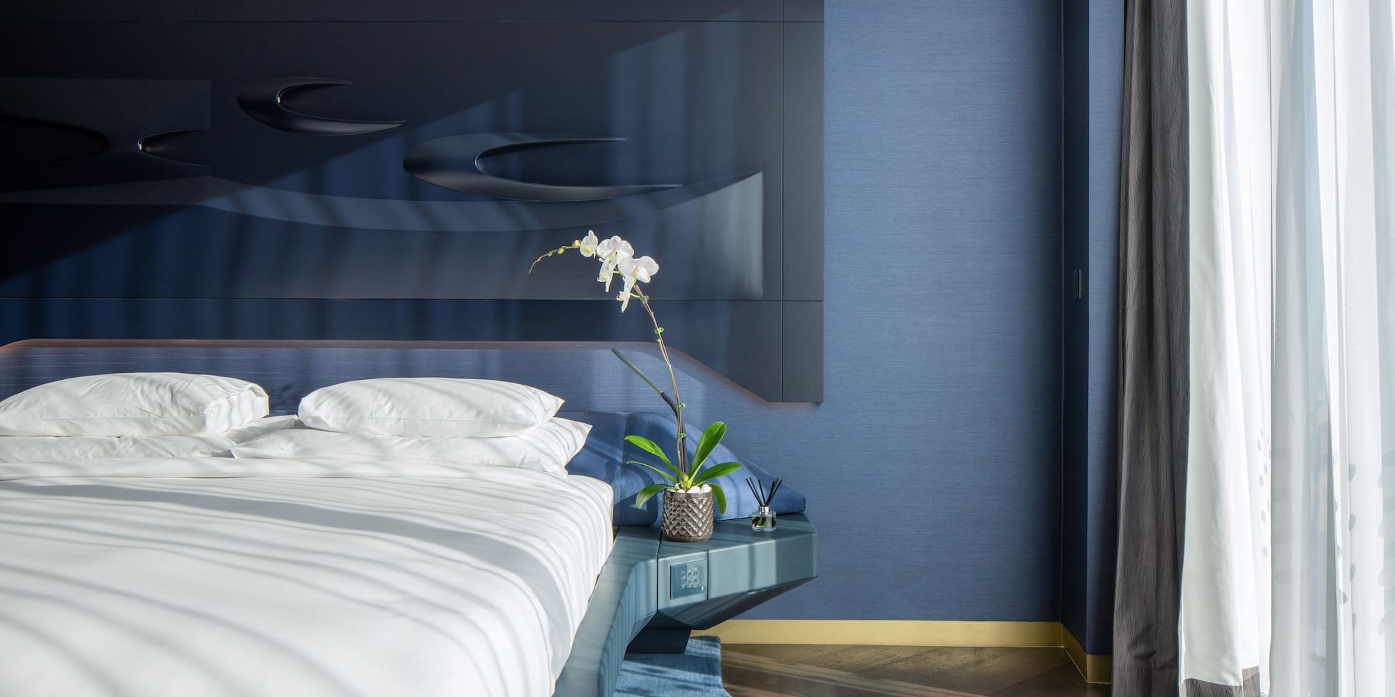 a bed with white sheets and pillows in a room with blue walls