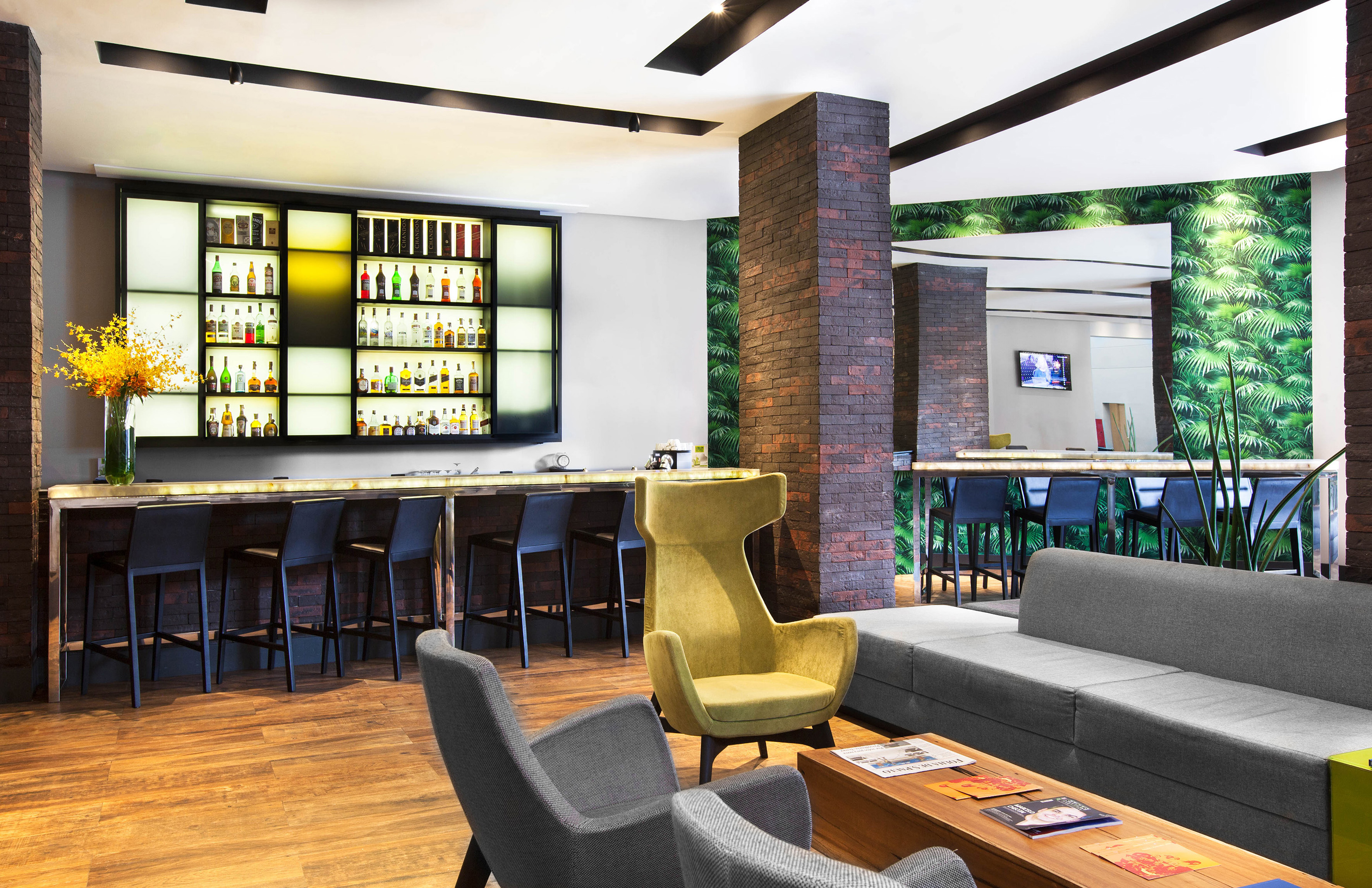 Modern hotel bar lounge with backlit liquor display, comfy seating, and tropical decor.