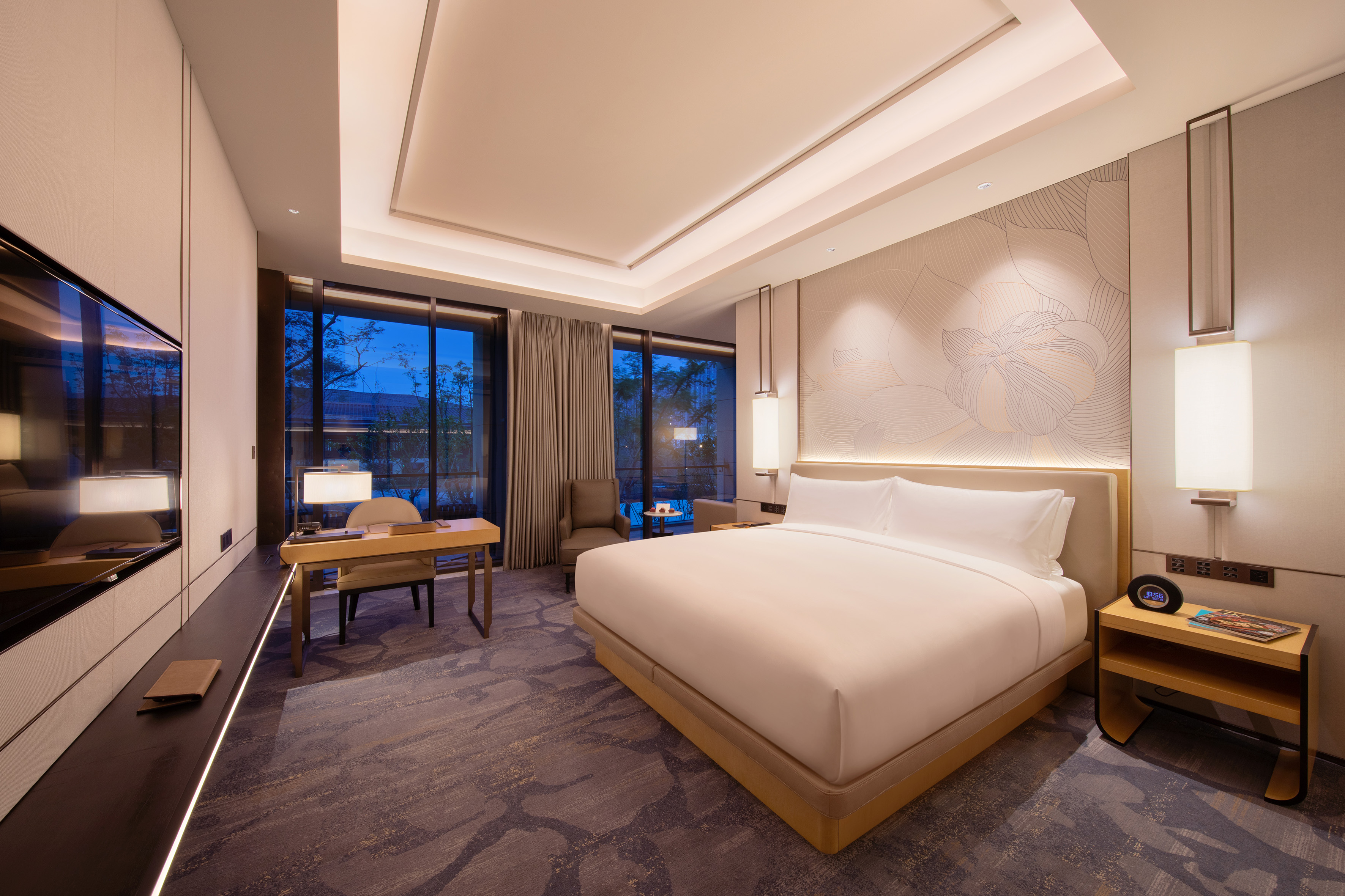 Modern hotel room with king bed, desk, large windows, and floral accent wall.