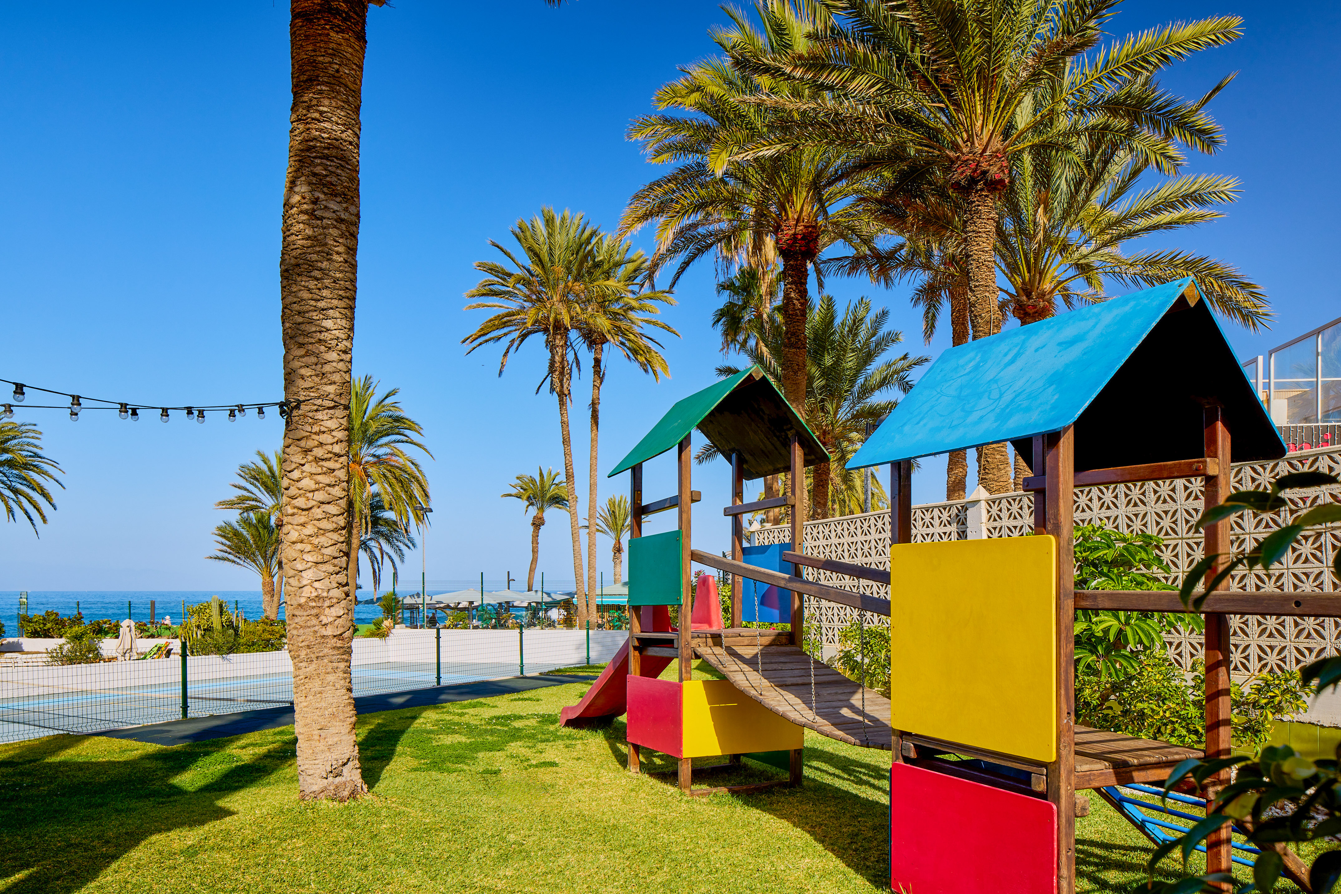 Colorful resort playground with palm trees, green grass, and ocean beyond.