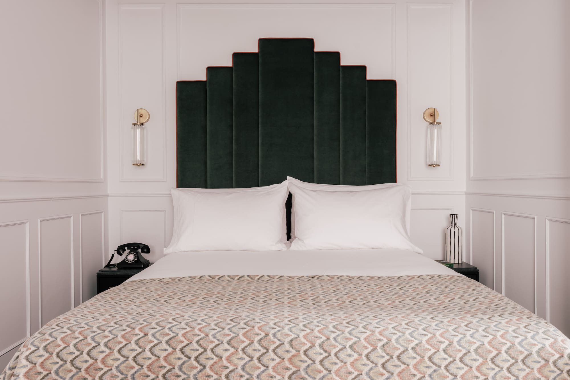 Luxury hotel bedroom with green velvet art deco headboard and patterned bedspread.