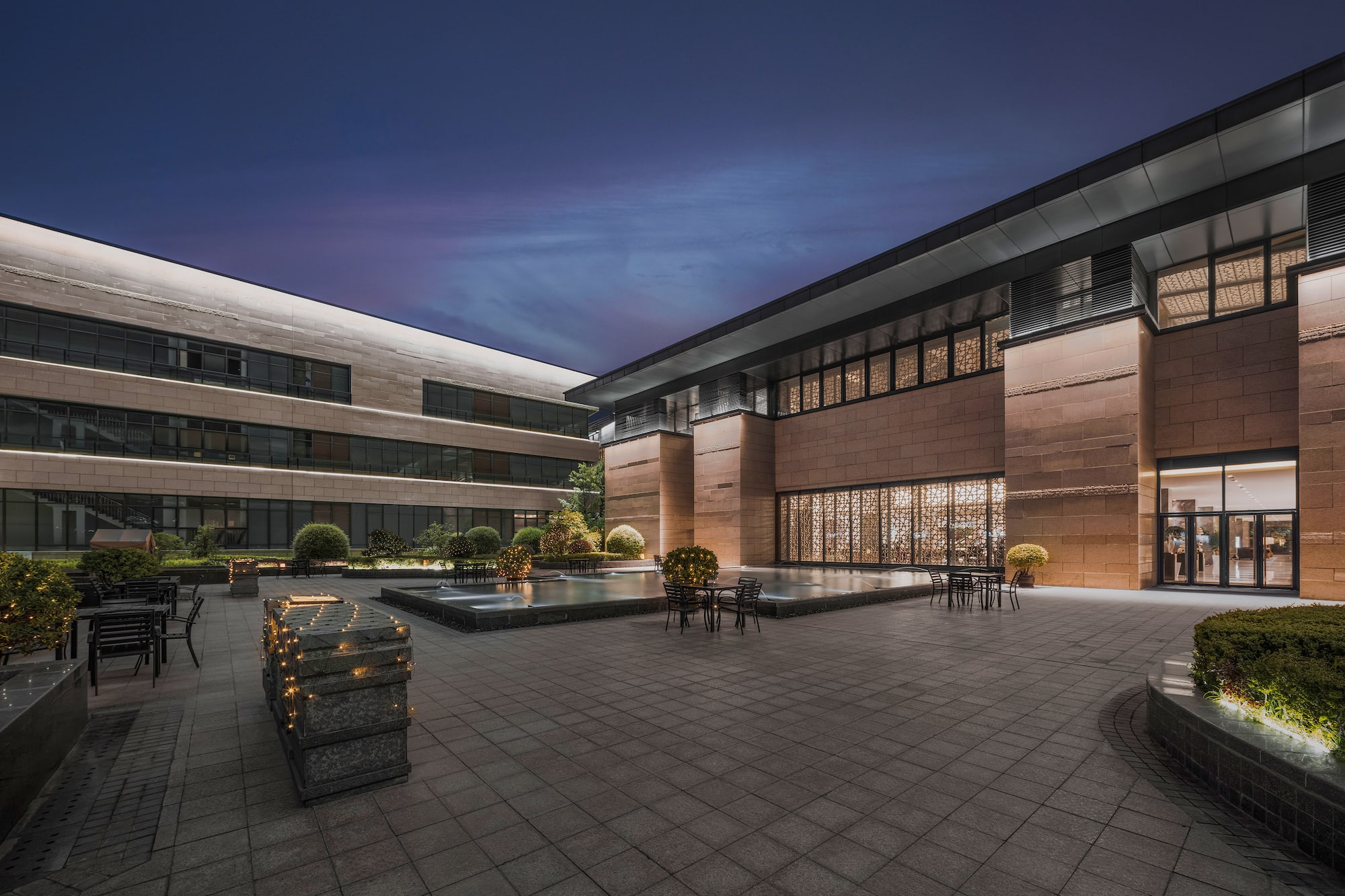 Illuminated modern building courtyard with water feature and outdoor seating.