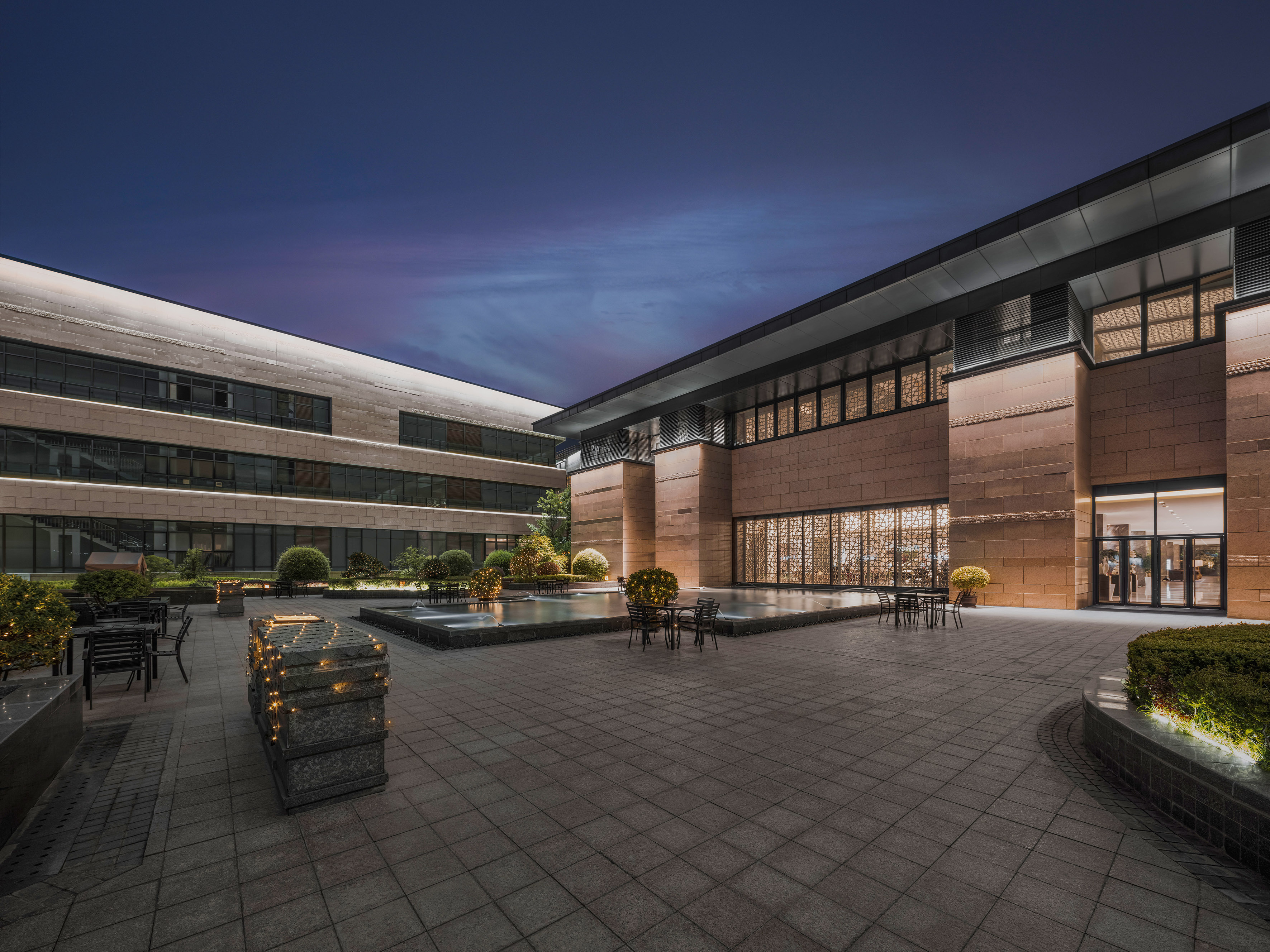 Illuminated modern building courtyard with water feature and outdoor seating.