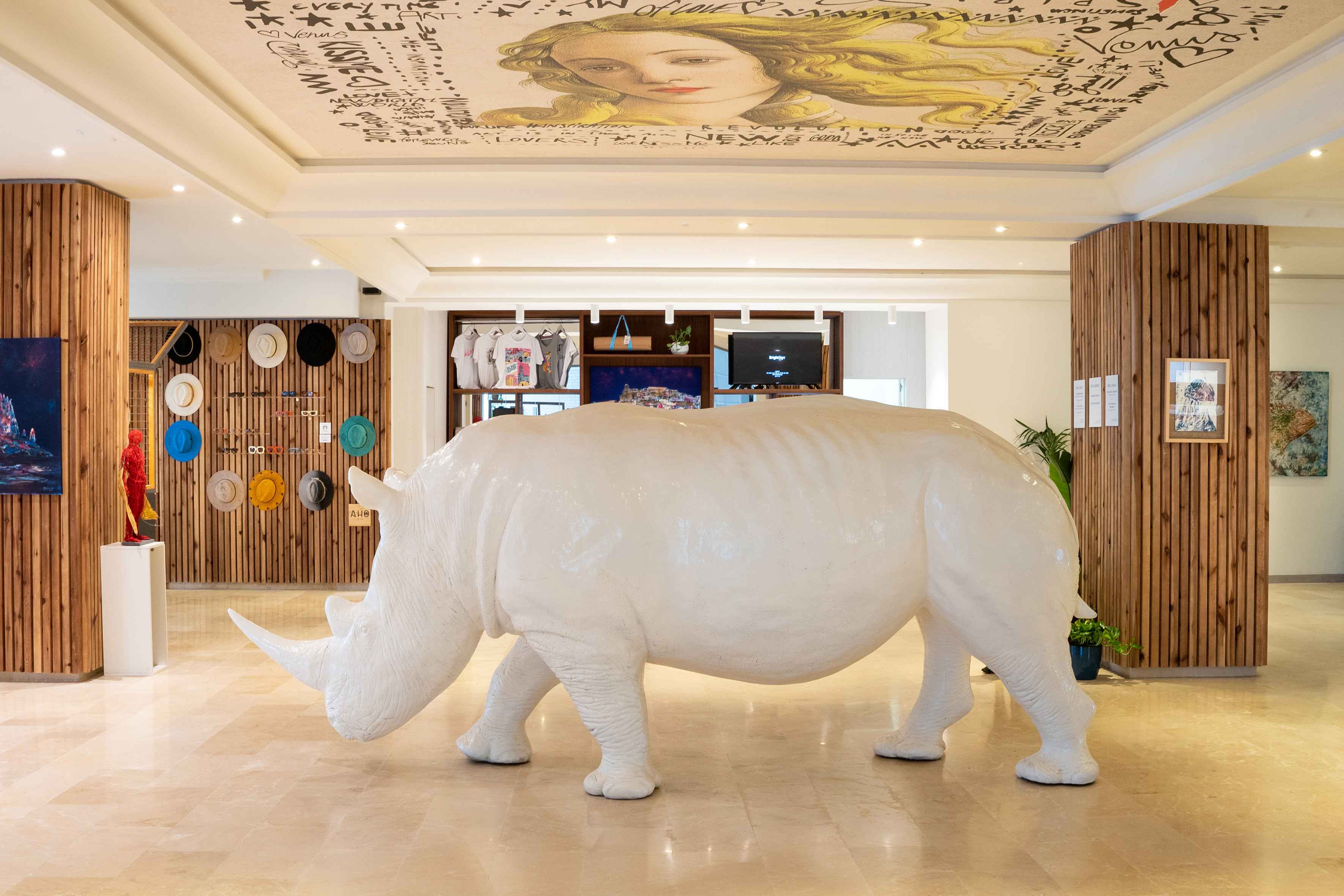 White rhinoceros sculpture in modern hotel lobby with ceiling art and retail display.