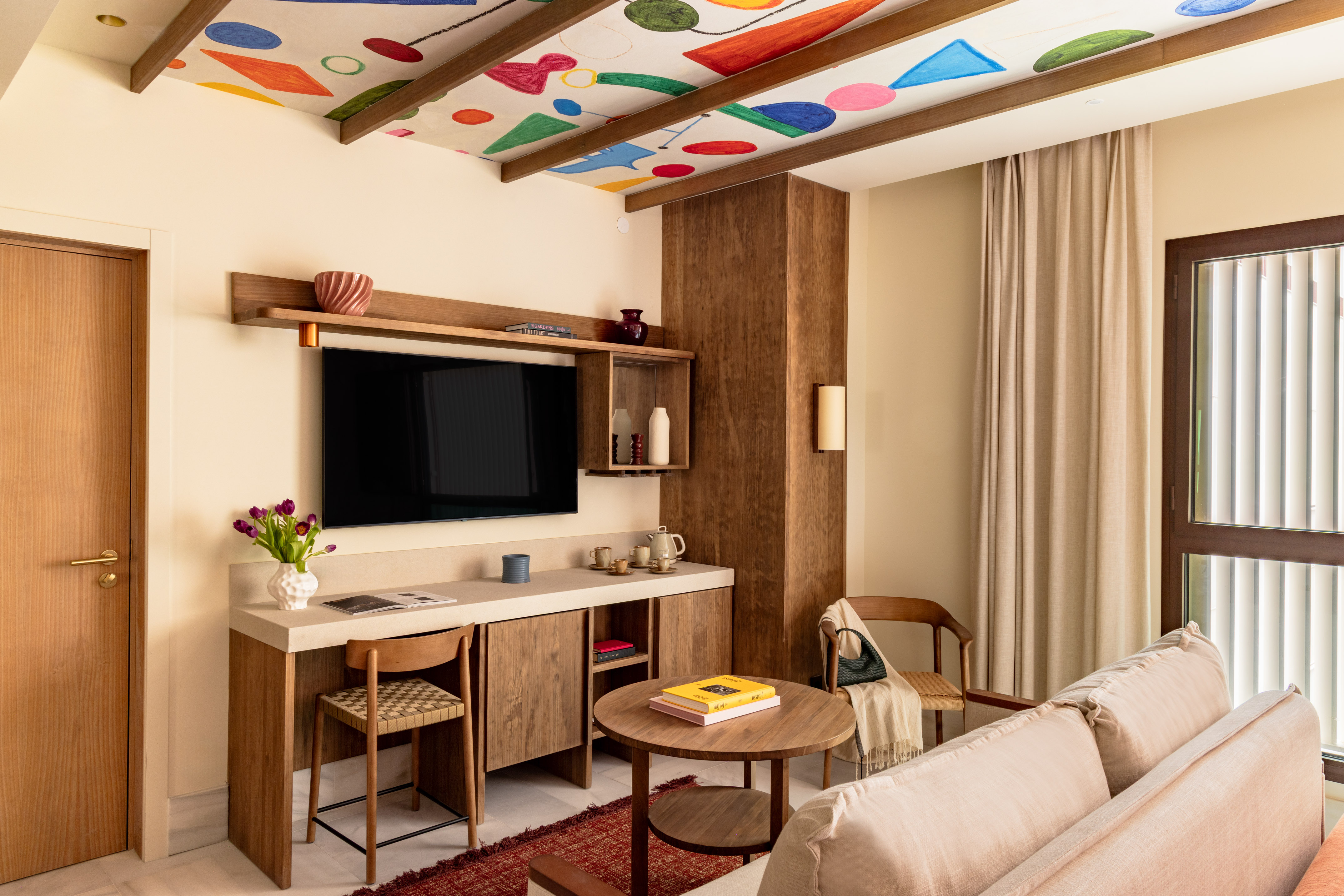 Modern living area with colorful abstract ceiling, wall-mounted TV, sofa, and wooden furniture.